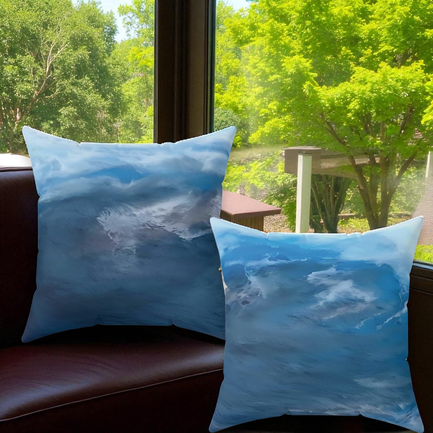 Two blue pillows with cloud pattern on a brown leather couch with a window view of green trees.