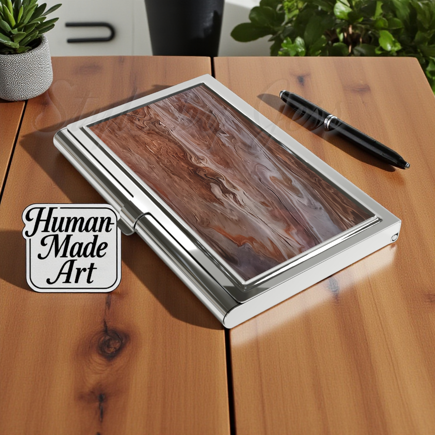 Wooden desk with a custom art image on a business card holder, pen, and 'Human Made Art' logo.