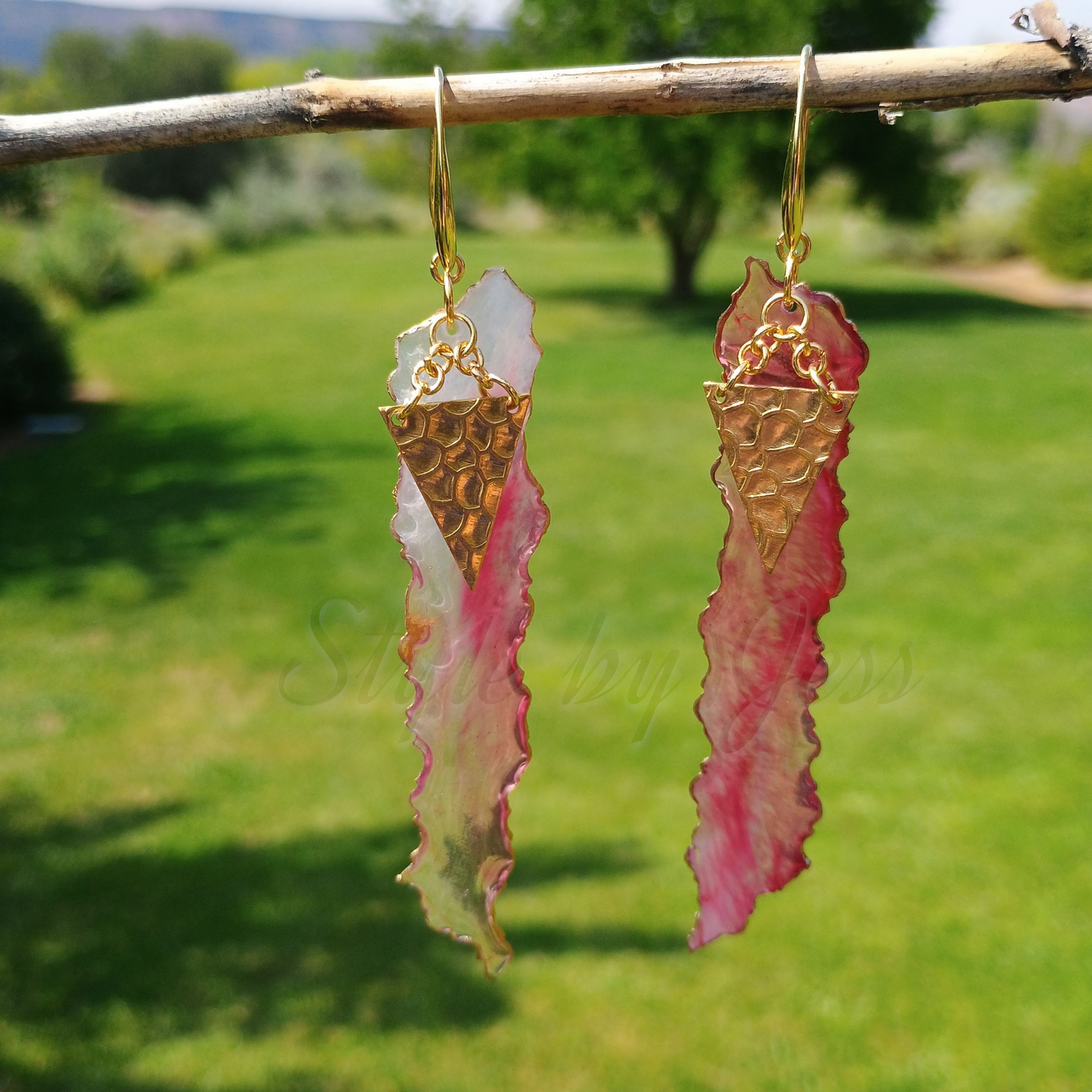 Pair of gold and pink earrings hanging from a branch with a garden background