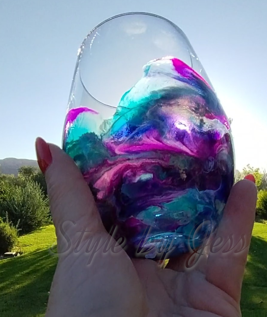 Colorful marbled glass stemless wine glass held by a hand with a blurred outdoor background