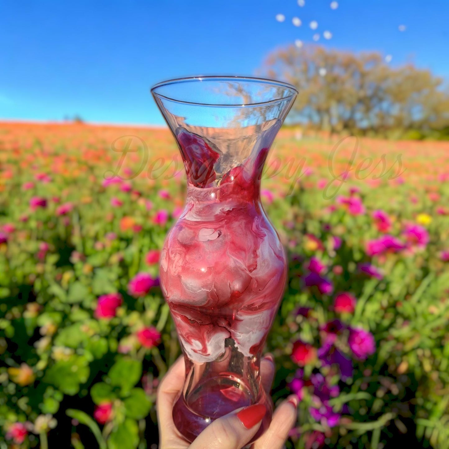 Glass vase with handmade resin art pink held in front of a colorful flower field perfect gift idea.