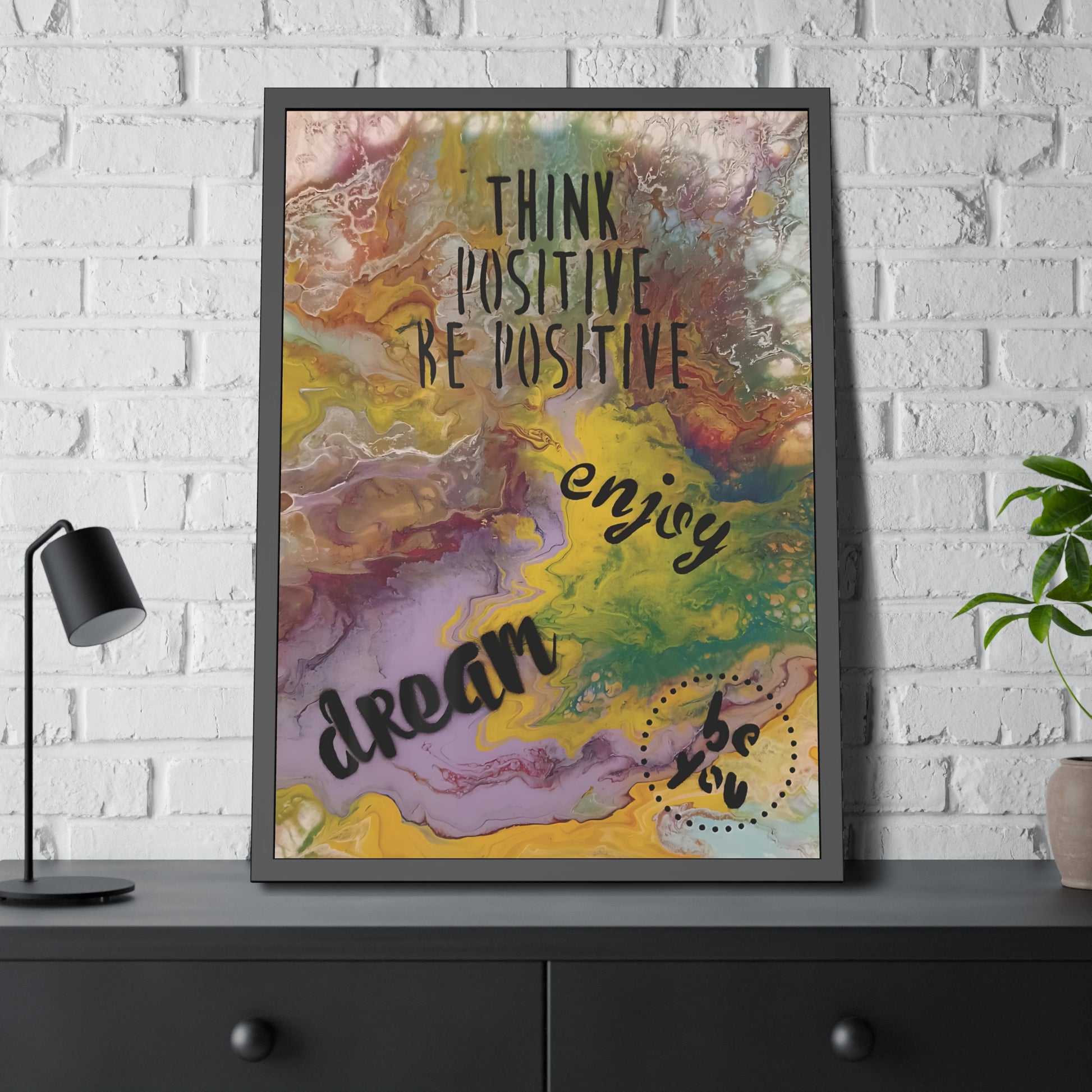 Framed motivational poster with colorful abstract design and text on a white brick wall background.
