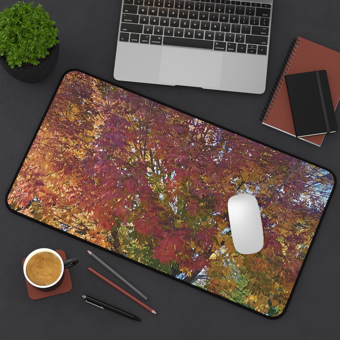 Desk setup with a colorful nature-themed mouse pad, laptop, mug, and stationery items.
