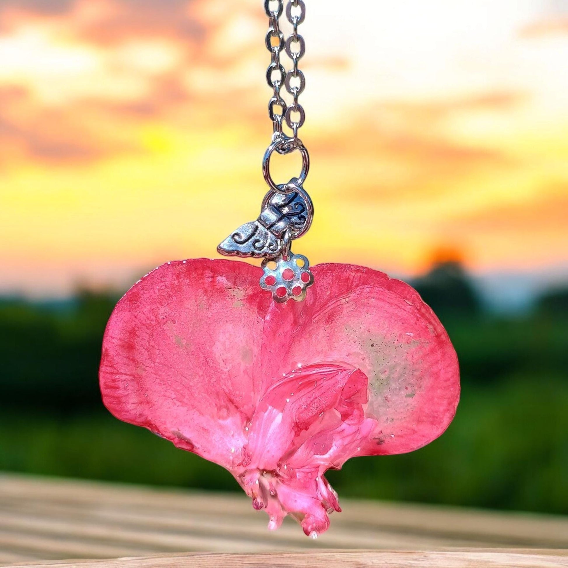 Pink flower petal heart-shaped pendant on a chain against a blurred natural background