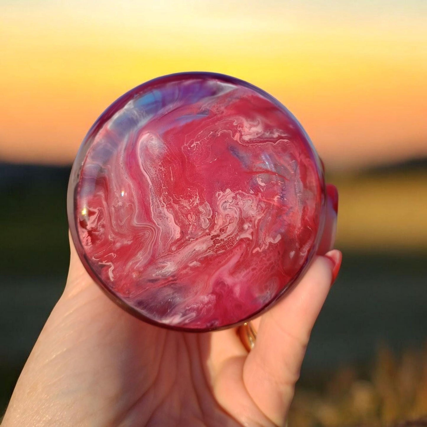 Image of bottom of glass vase with a hand holding it with a blurred natural background