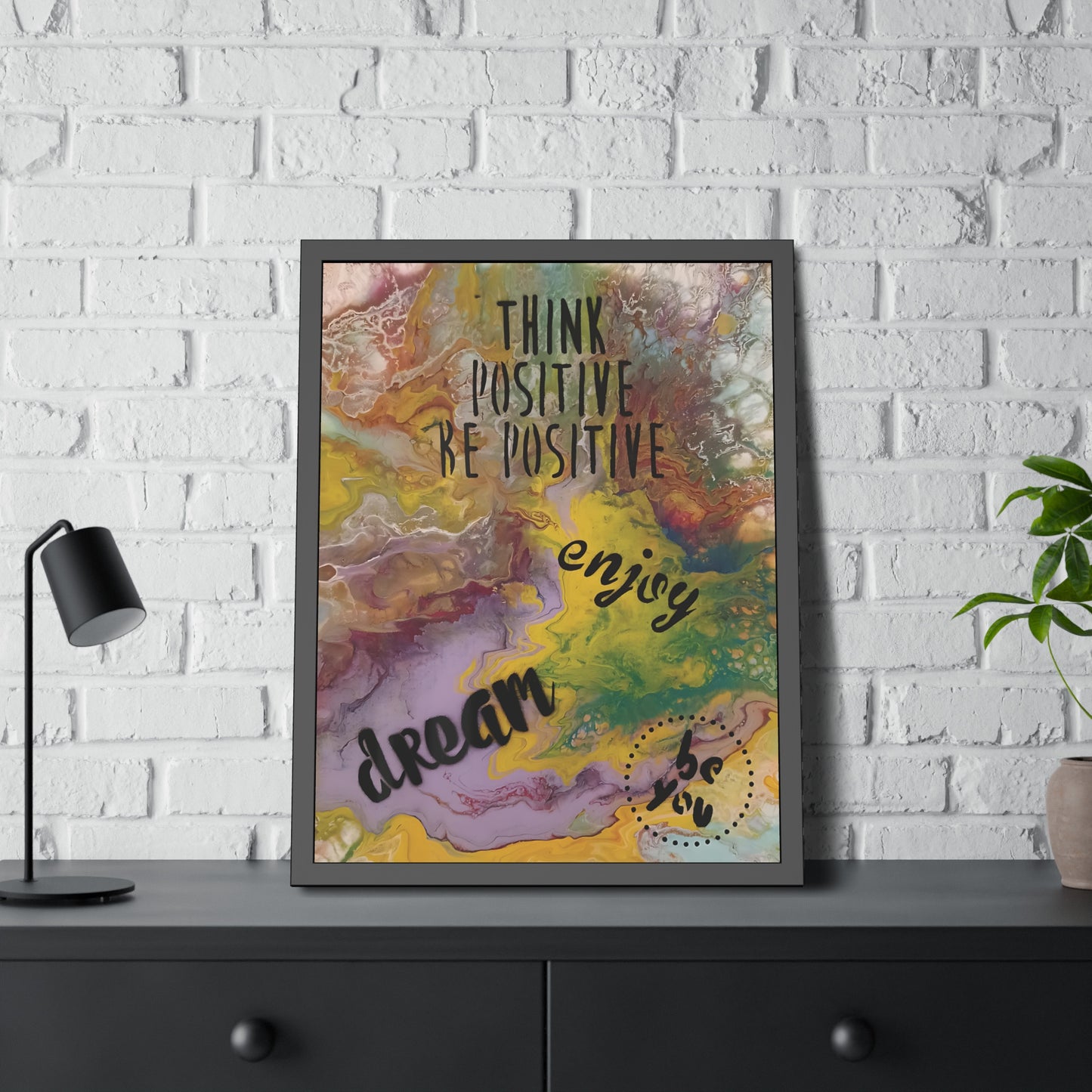 Framed motivational poster with colorful abstract design and text on a white brick wall.