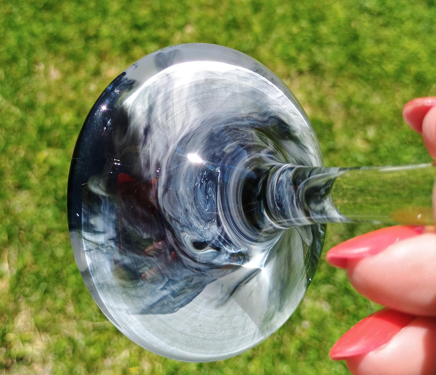 Close-up of bottom of a wine glass with swirling liquid against a blurred green background by Style By Jess