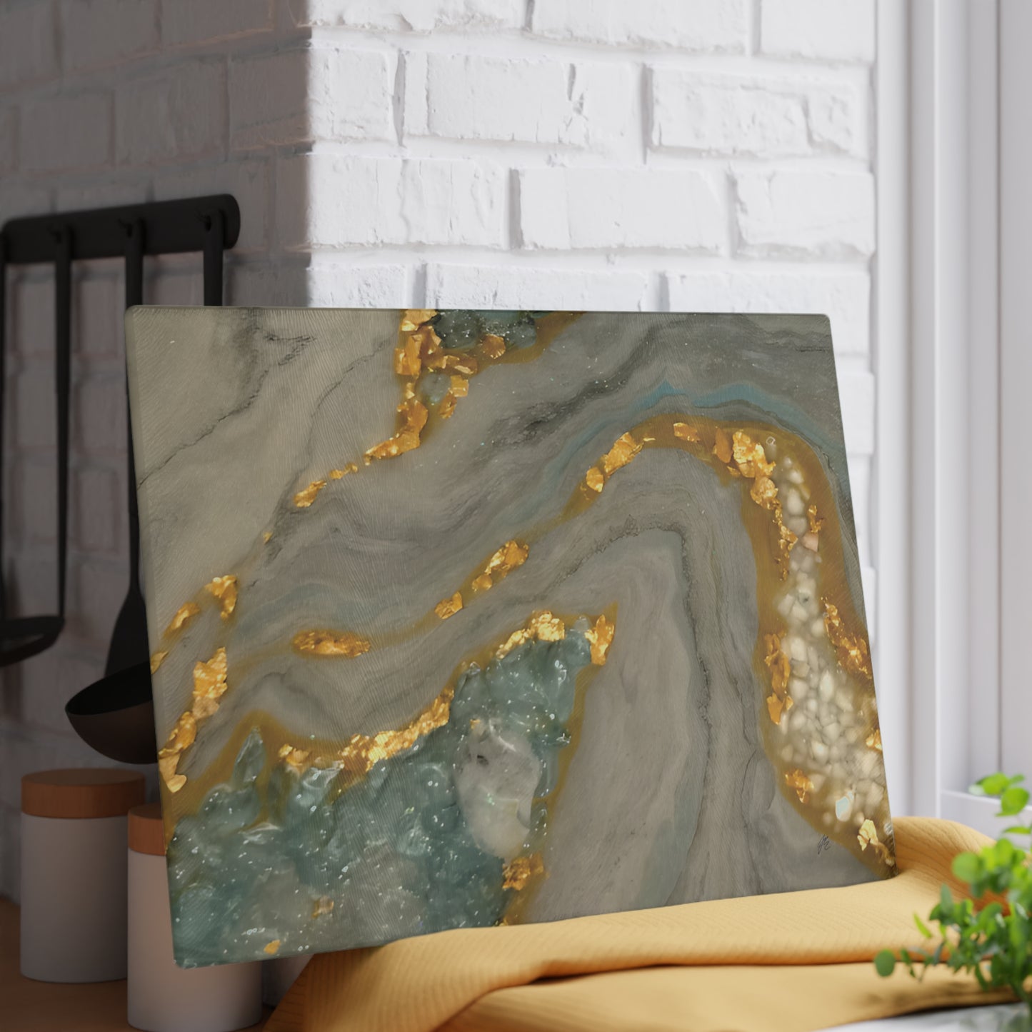 Decorative glass cutting board propped up on a wall with gold and gray abstract design on a white brick wall background