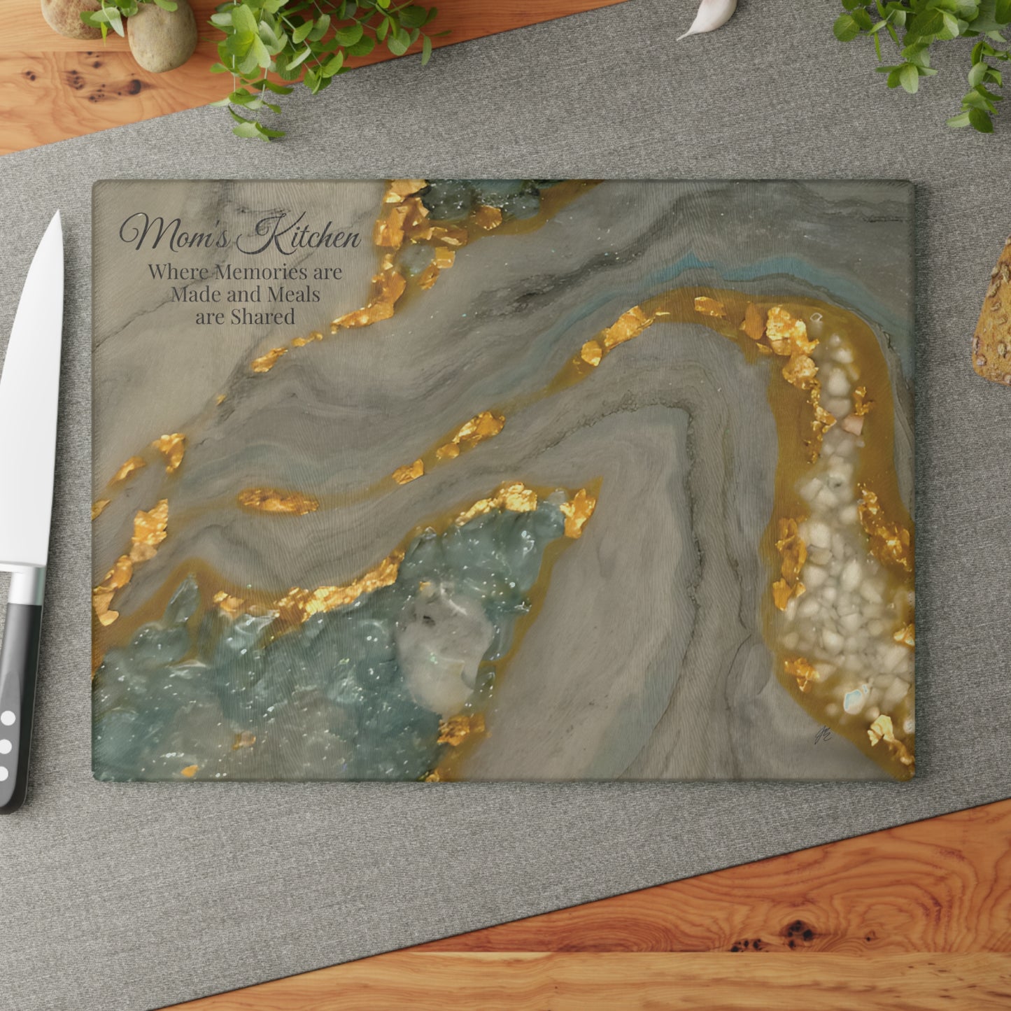 Marble-patterned cutting board with gold accents on a gray surface, featuring text 'Mom's Kitchen'.