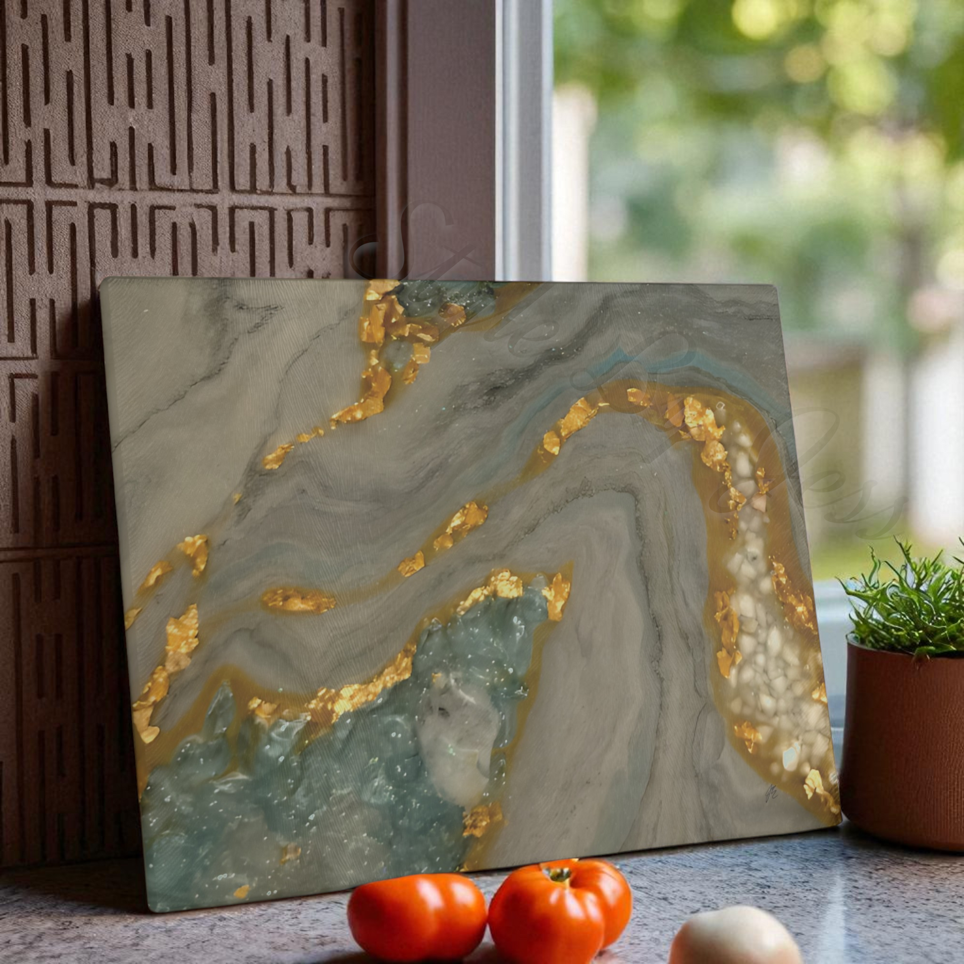 Decorative cutting board with gold accents on a counter with tomatoes and an onion.