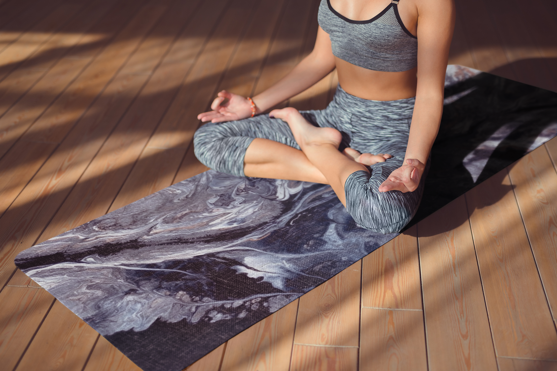 Person in gray athletic wear sitting on a marble-patterned yoga mat on a wooden floor.