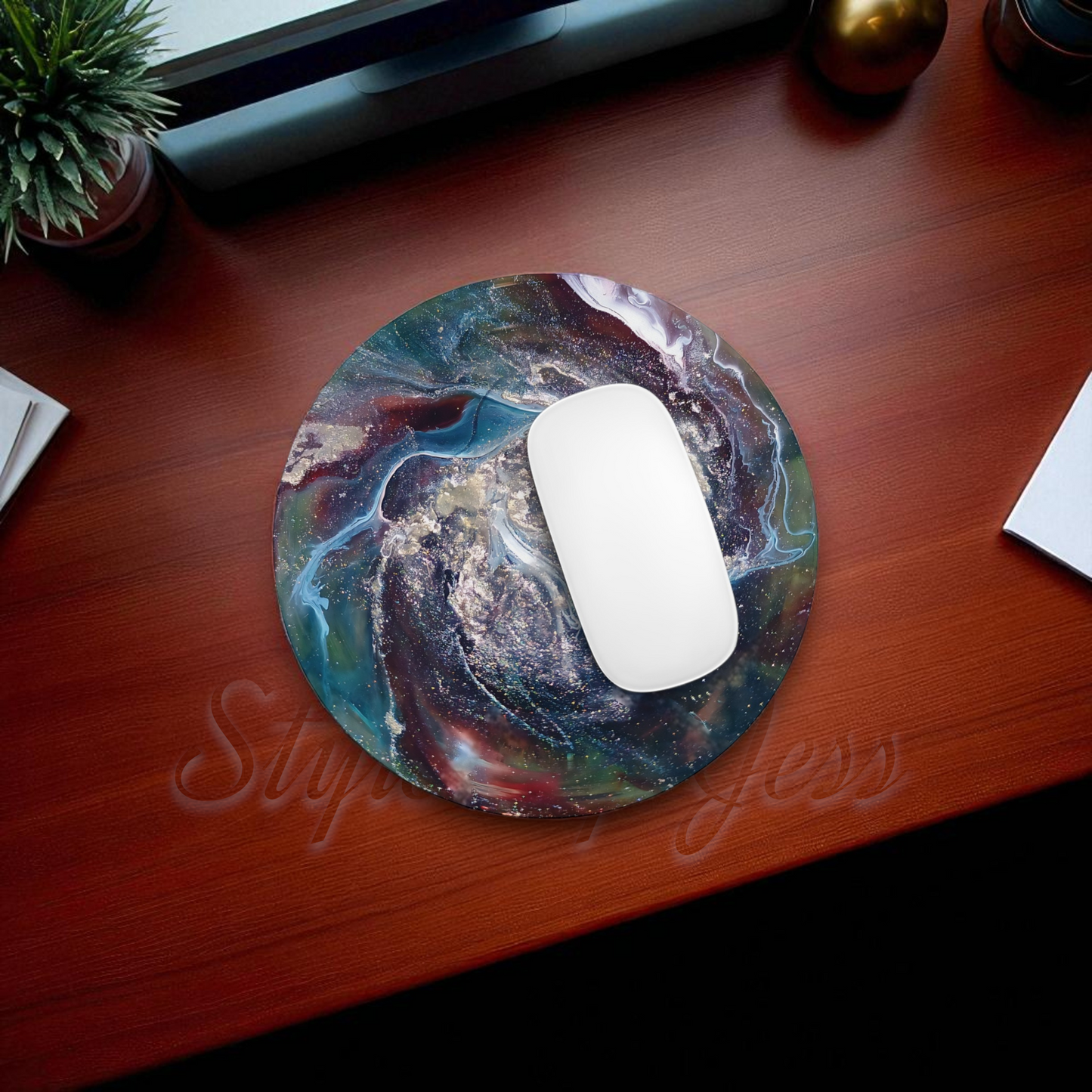 Mouse on a colorful mouse pad on a wooden desk with a plant and office items.