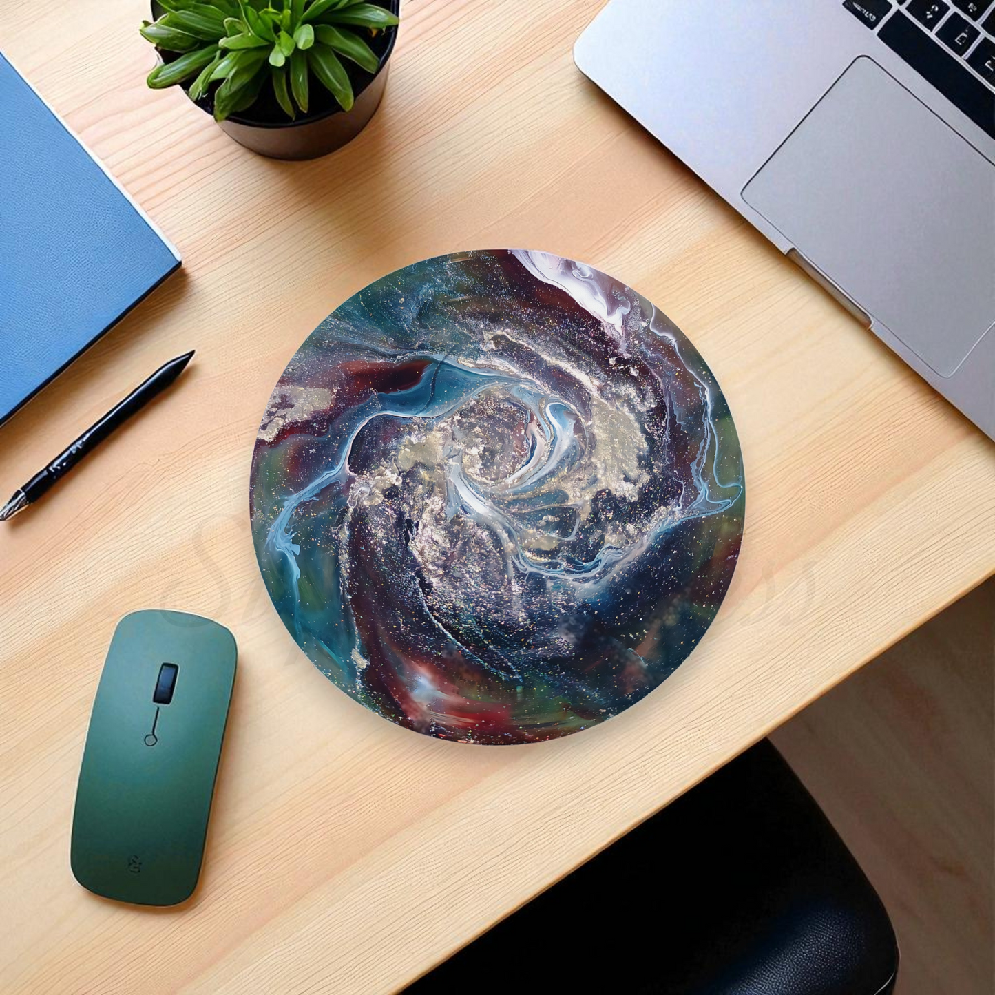 Round mouse pad with artistic design on a wooden desk with laptop, pen, and plant.