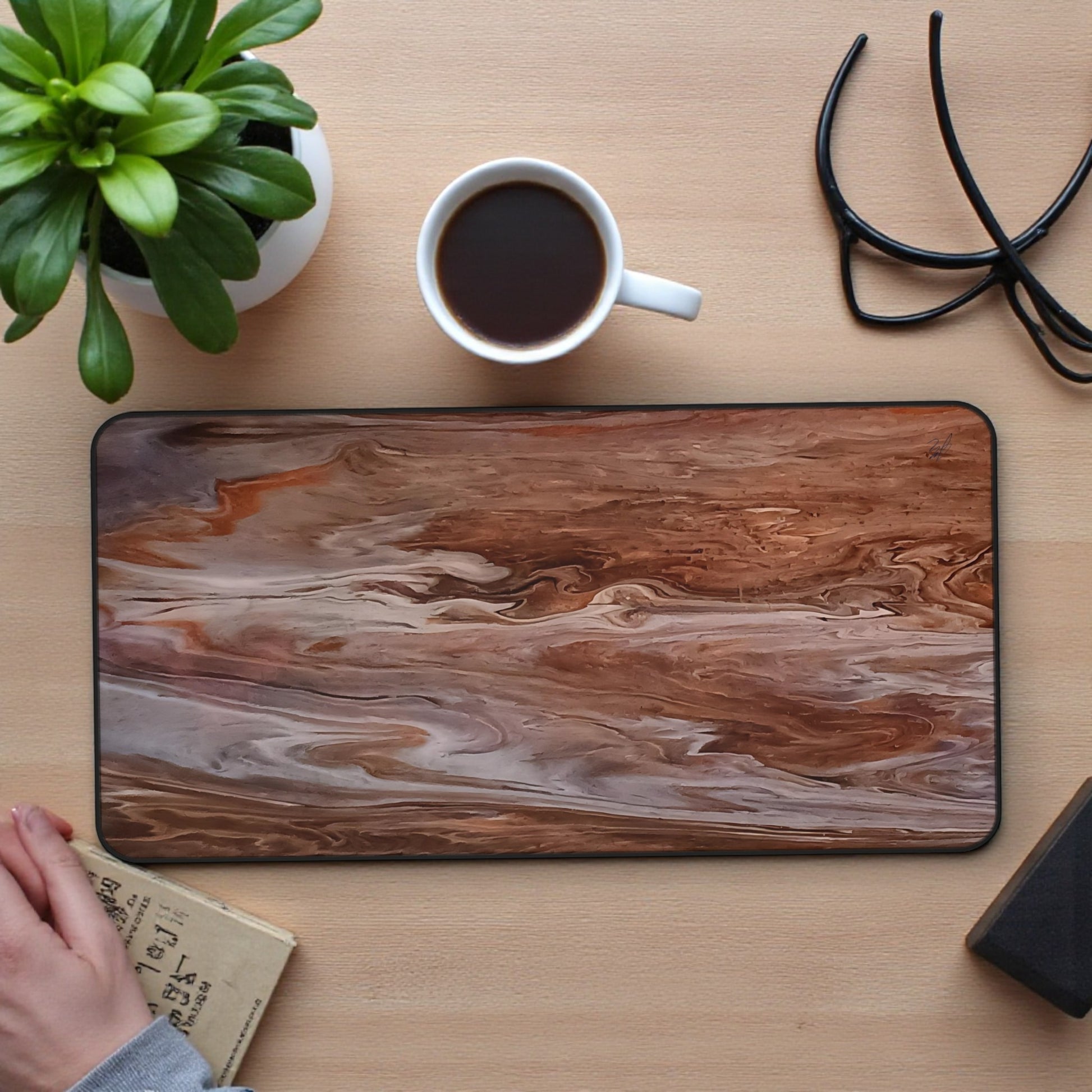 Marble-patterned mouse pad on a wooden desk with a cup of coffee, plant, and books.