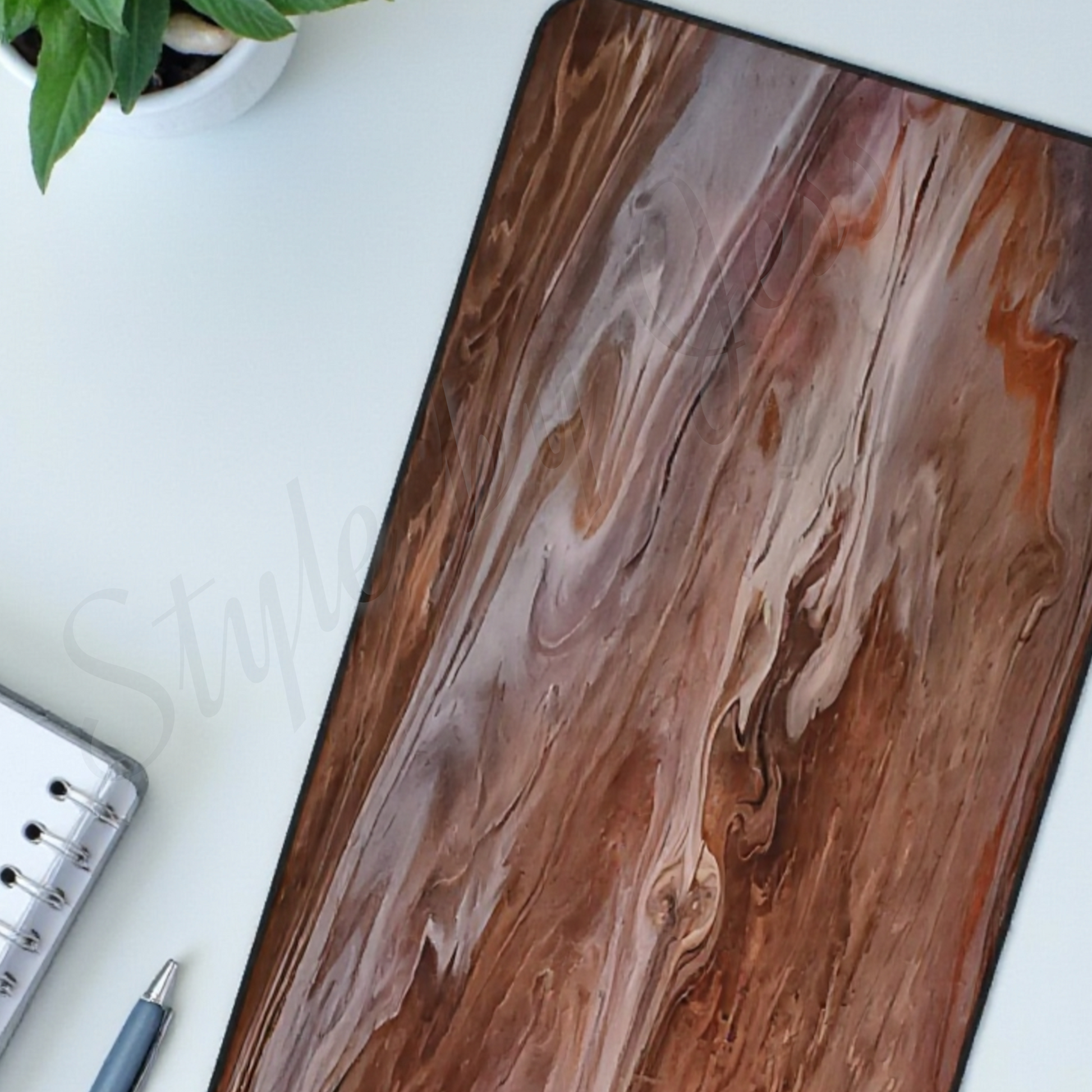 Oversized Desk Mat with a marbled image from an original art painting sitting on a white desk with a plant an d notepad in the background. 