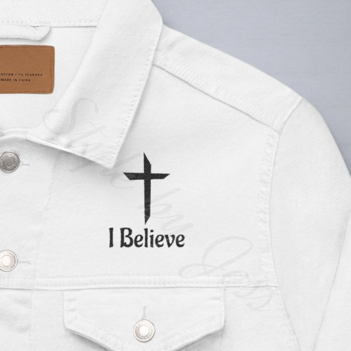 White denim jacket with a cross and 'I Believe' text on a gray background