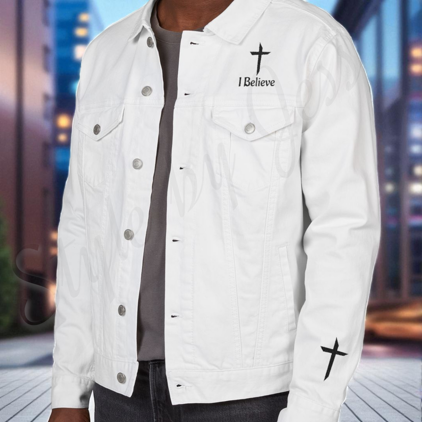 White denim jacket with 'I Believe' and cross design on a blurred cityscape background