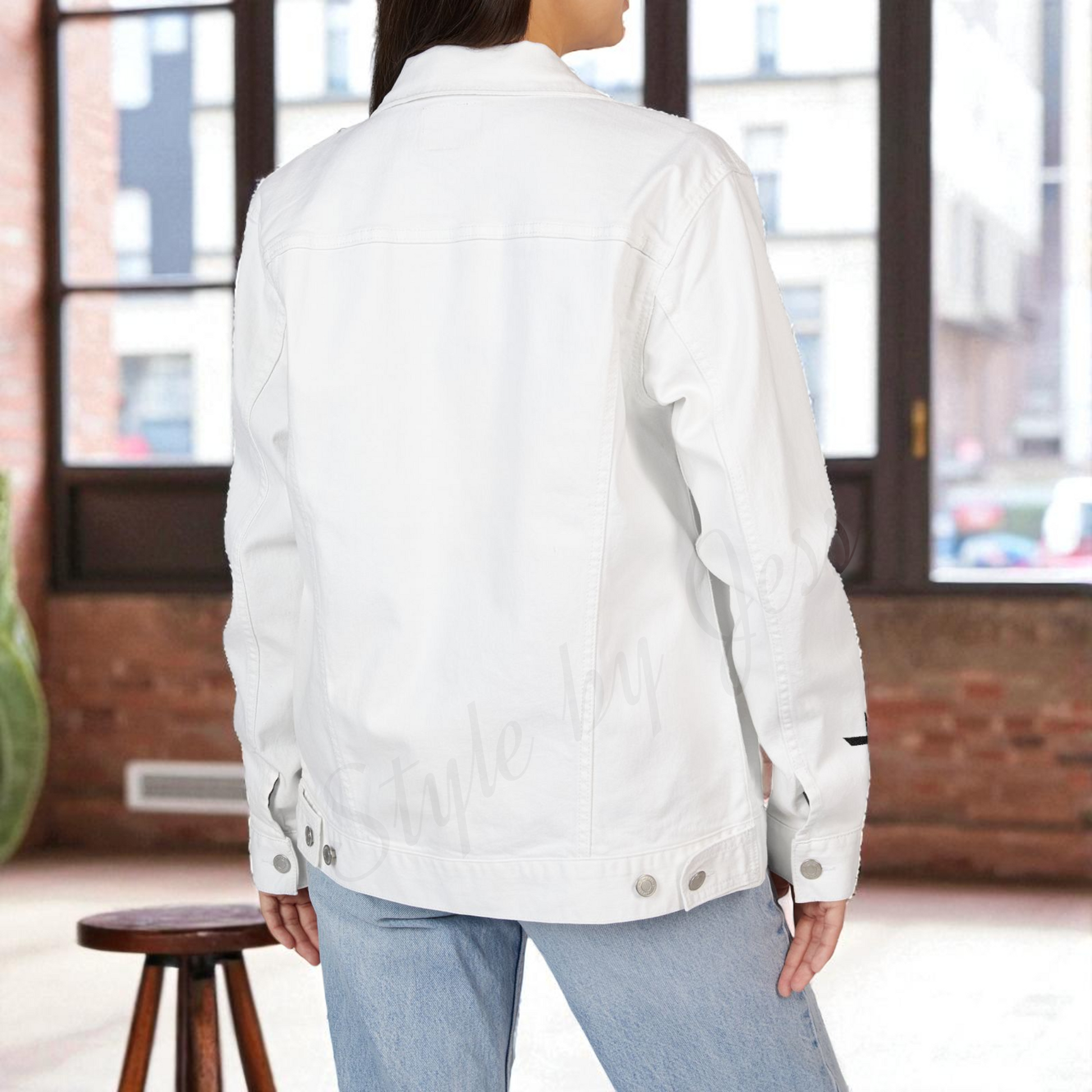 Person wearing a white denim jacket indoors with a brick wall and window in the background