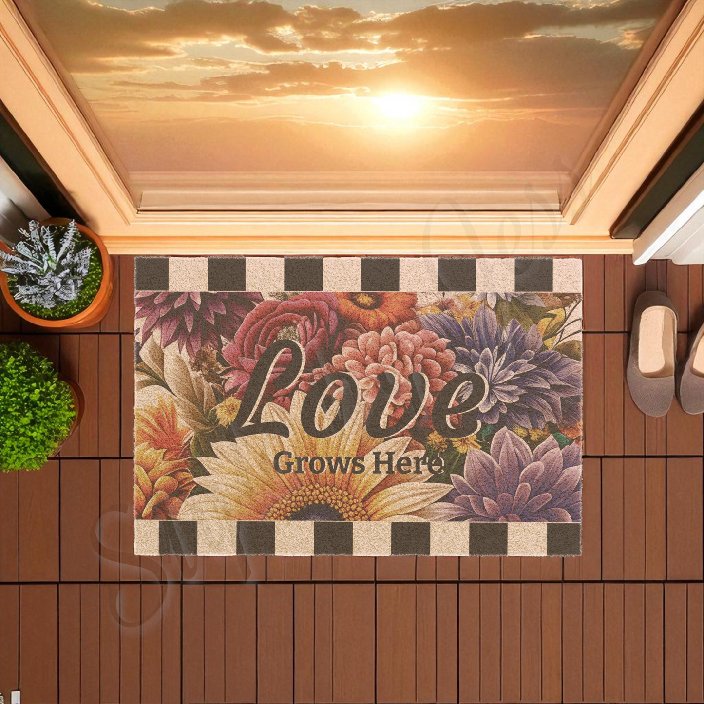 Decorative doormat with floral design and 'Love Grows Here' text on a wooden deck with a sunset view.