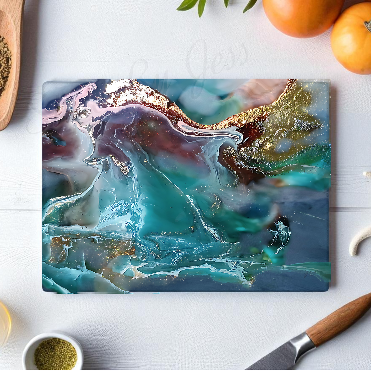 Glass cutting board with teal and turquoise colors on a white table with oranges in the background. 