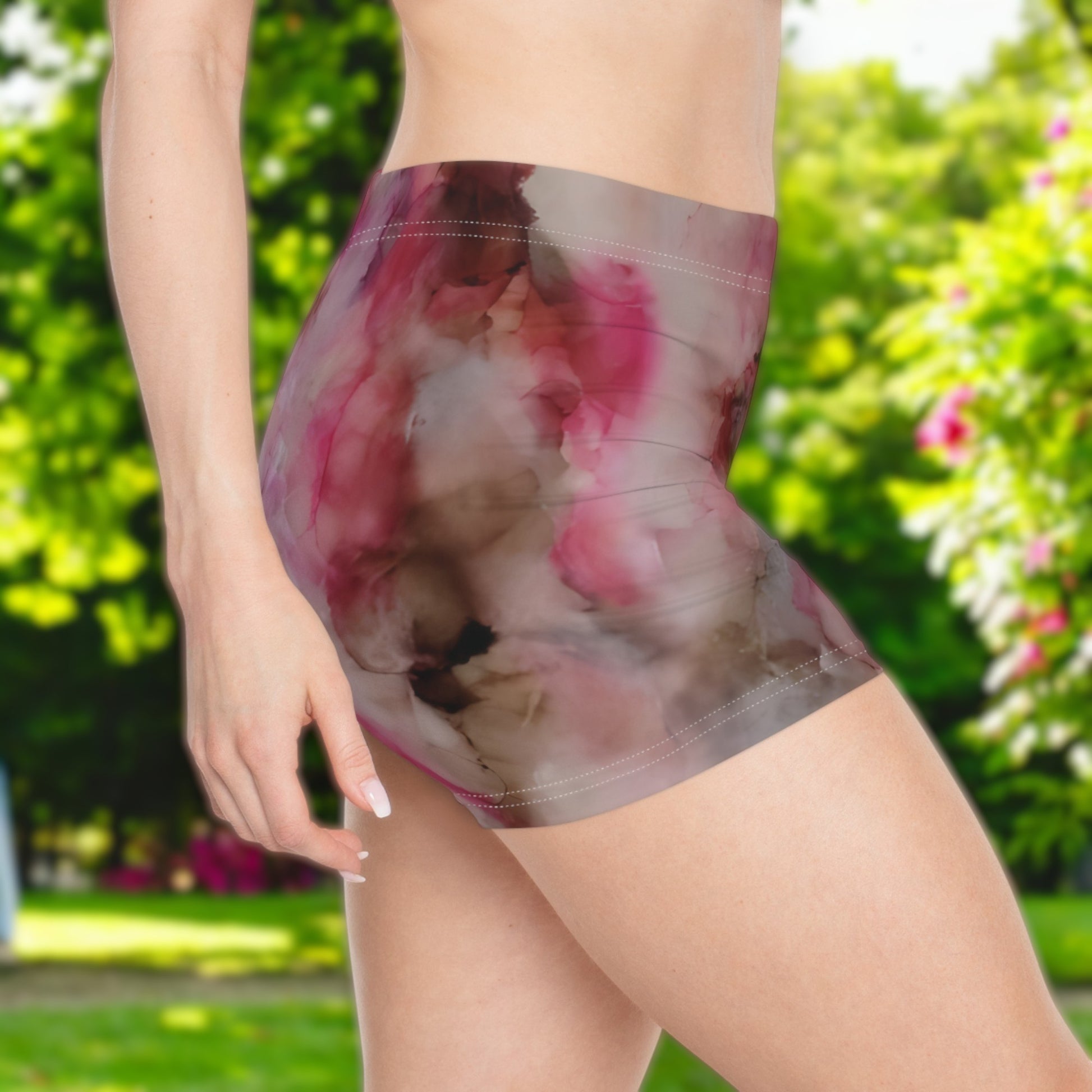 Person wearing a colorful pink and gray -patterned booty shorts set with a blurred green outdoor background