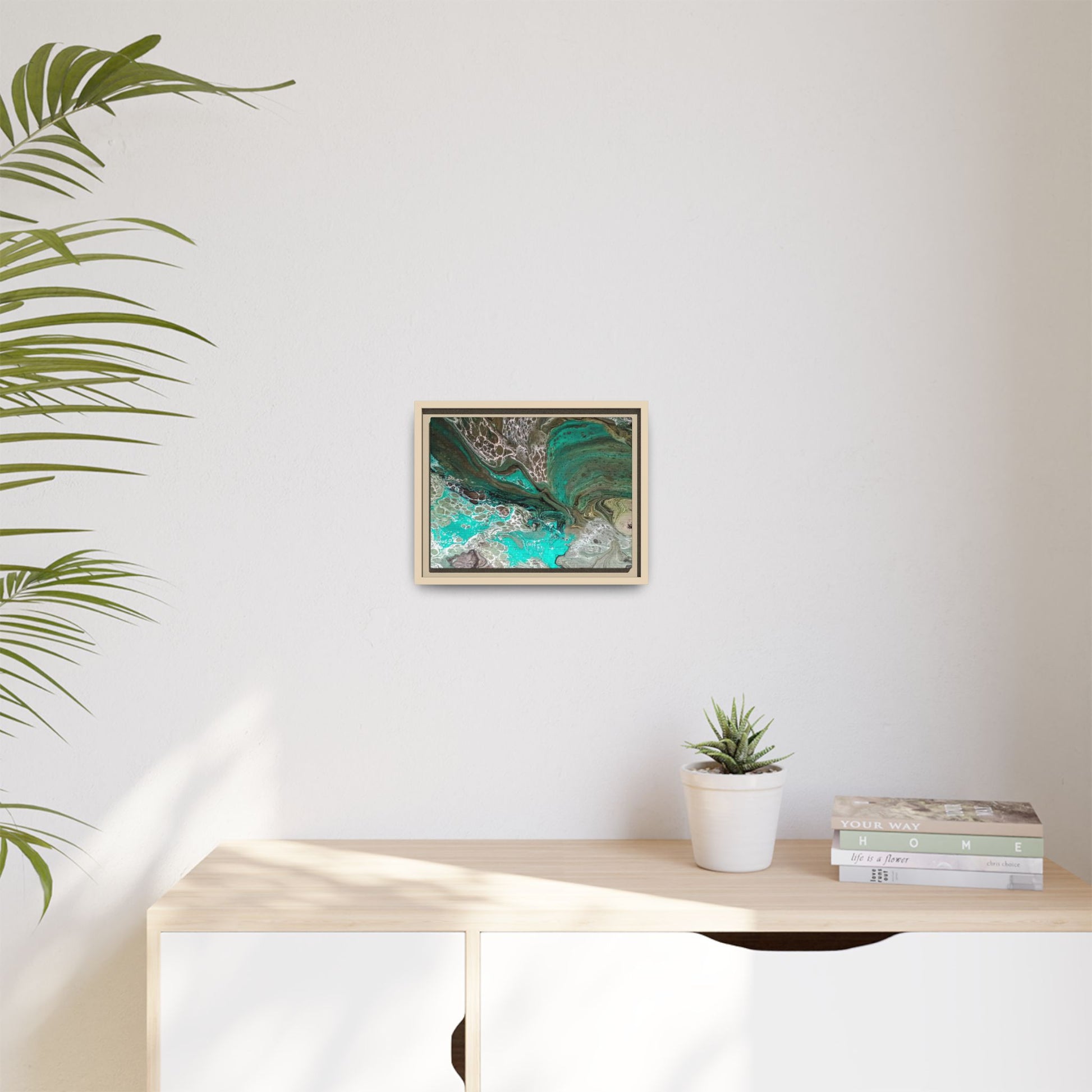 Framed artwork on a wall above a desk with a plant and books displayed in an office setting.