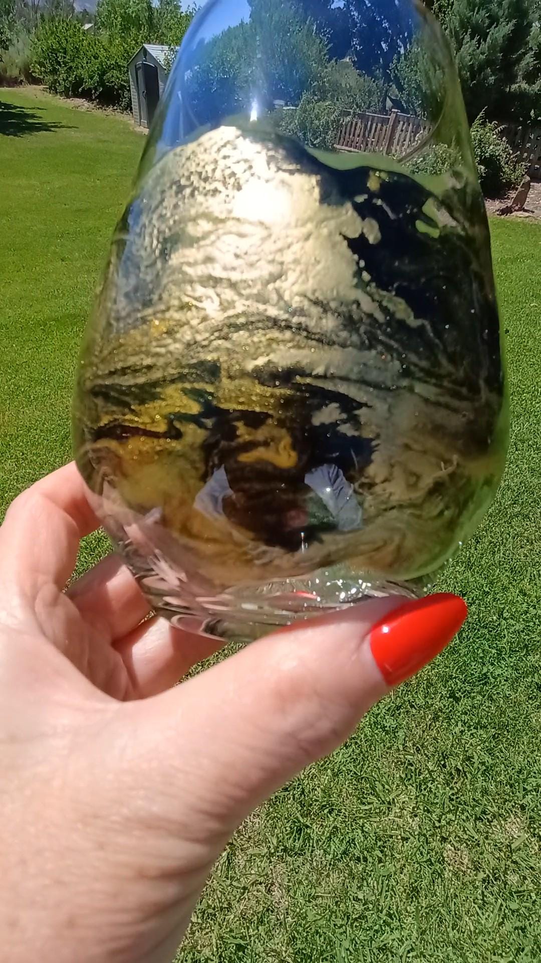 Hand holding a stemless wine glass with abstract design, outdoors on grass