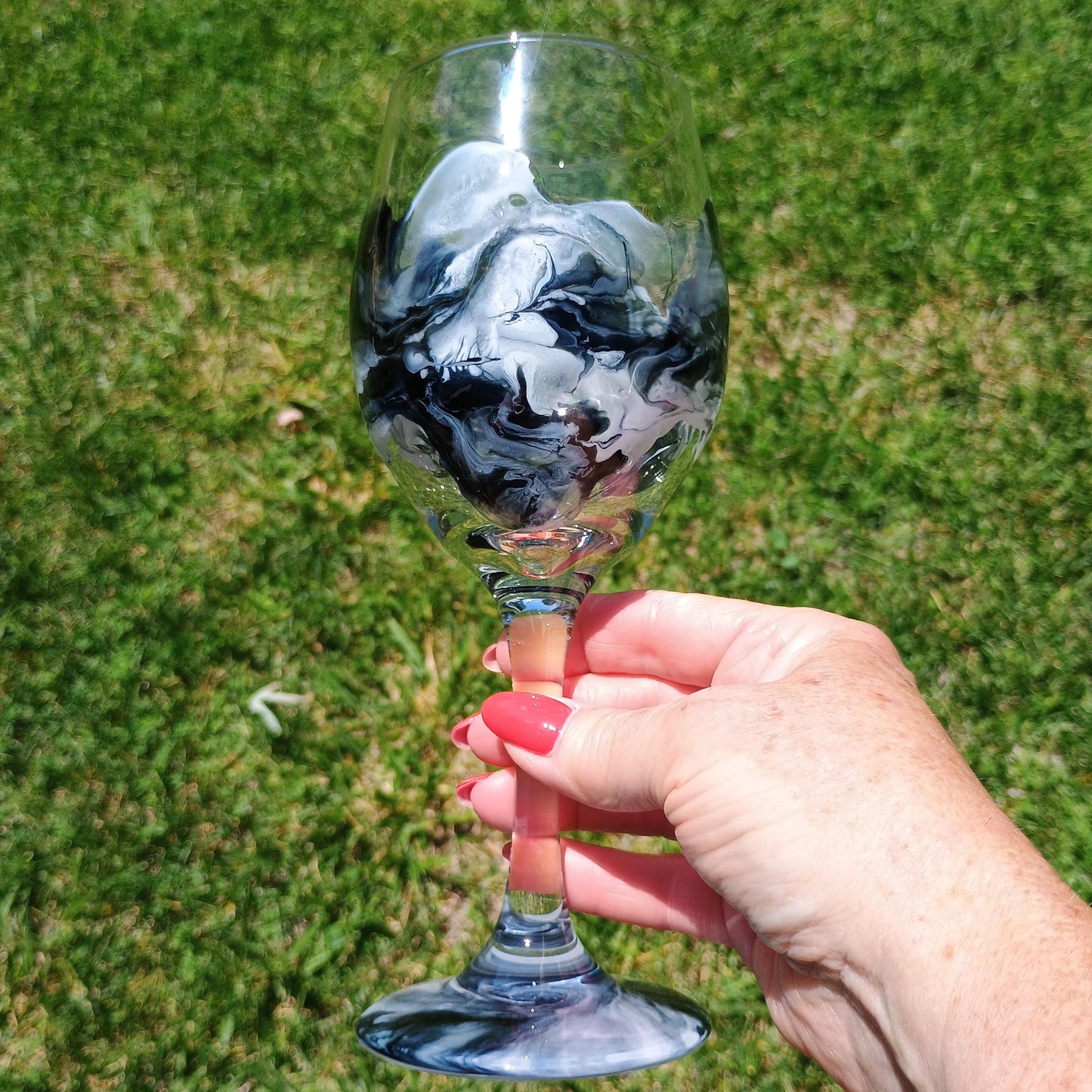 Hand holding a marbled wine glass against a grassy background by Style By Jess