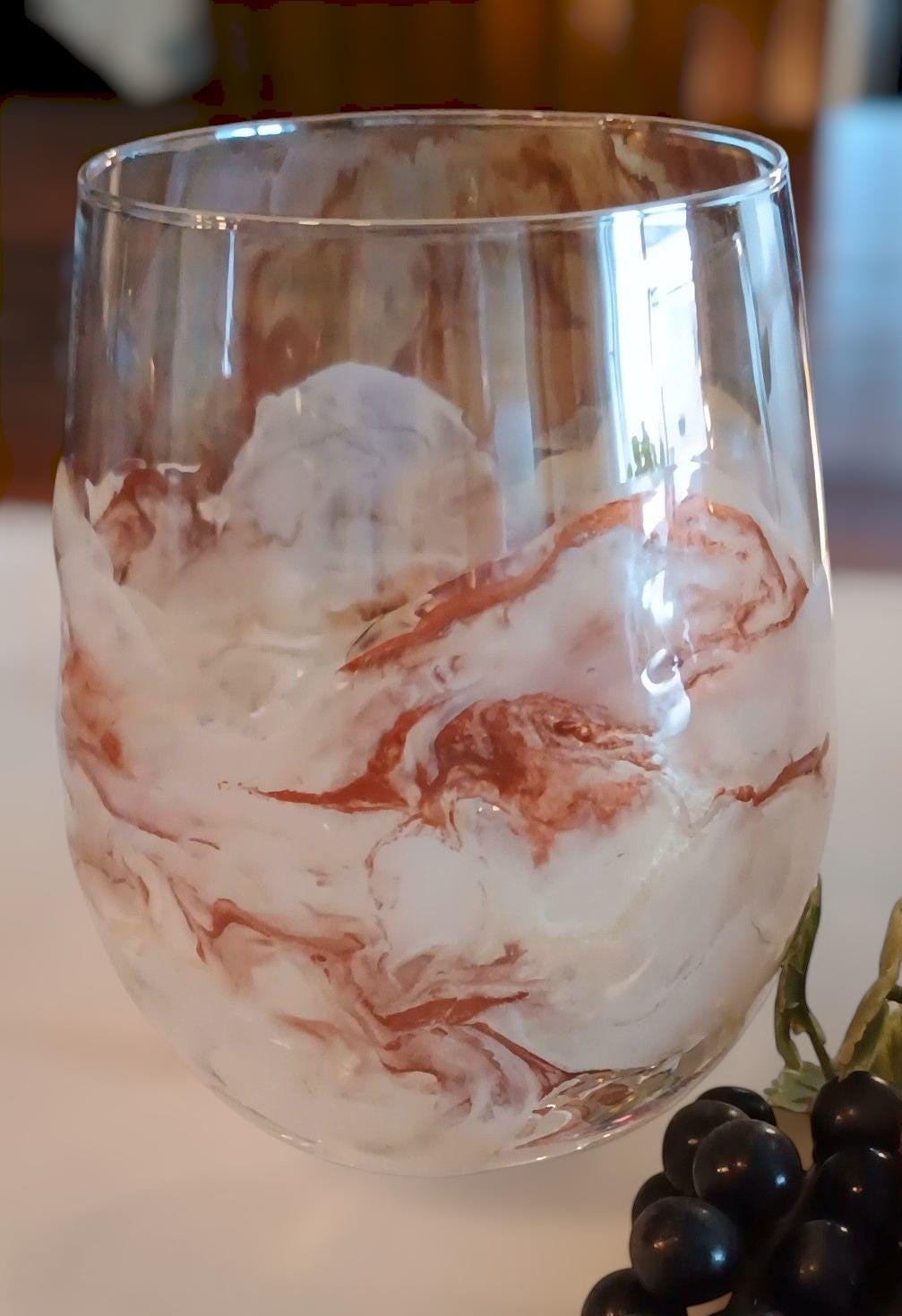 Marbled glass wine glass on a white surface with grapes in the background