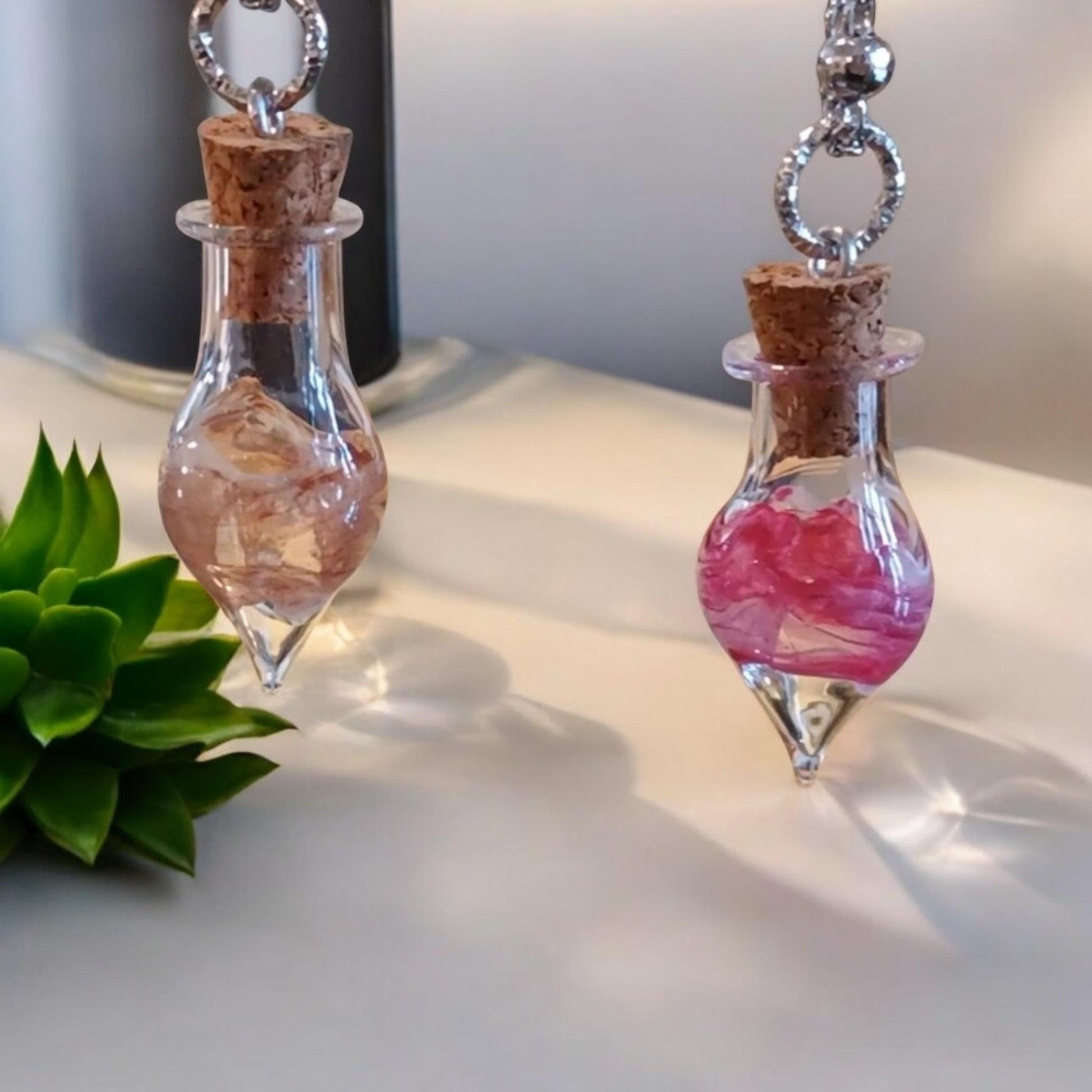 Glass bottle pendant necklace with cork stoppers on a white surface with a plant in the background