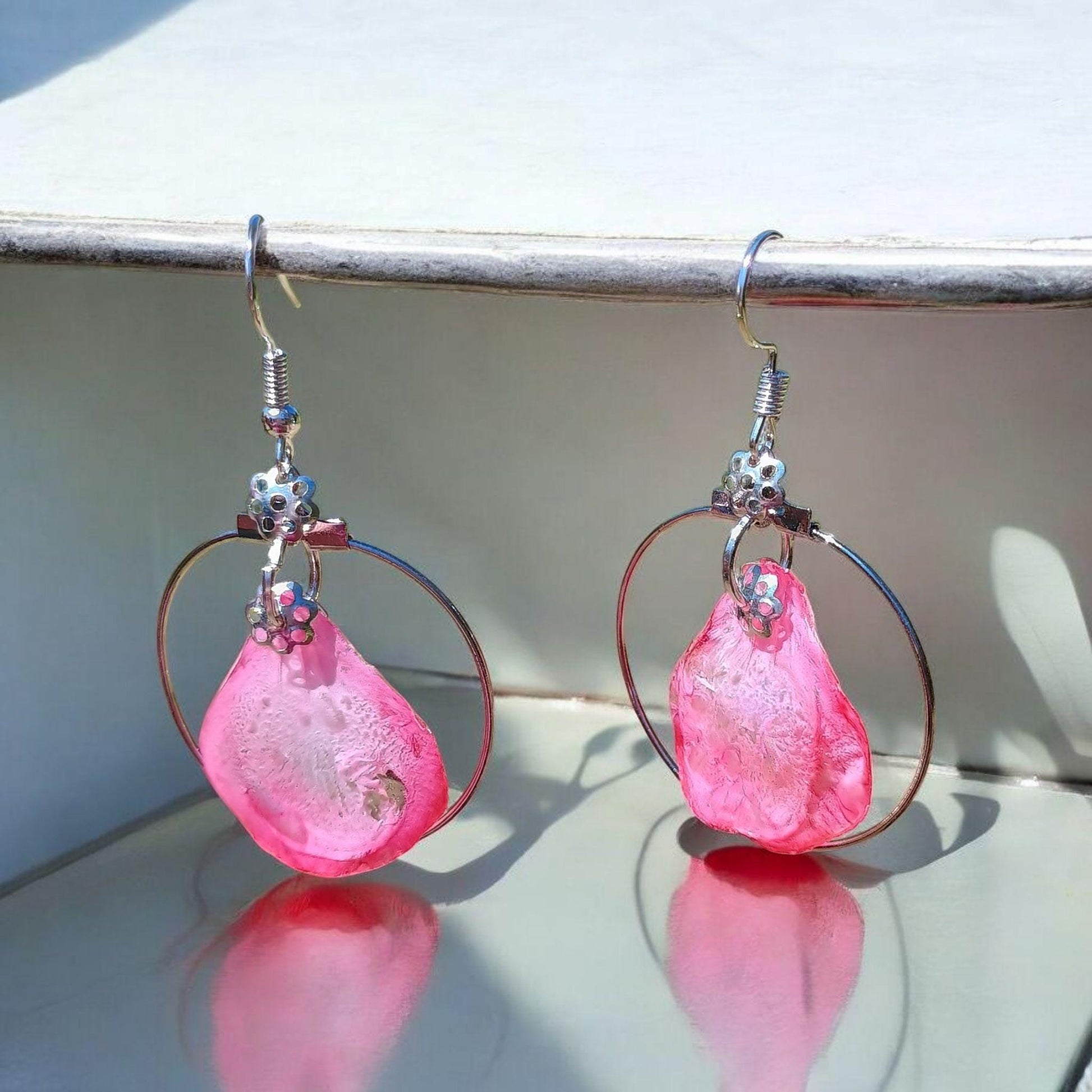 Pink teardrop earrings with silver loops on a reflective surface.