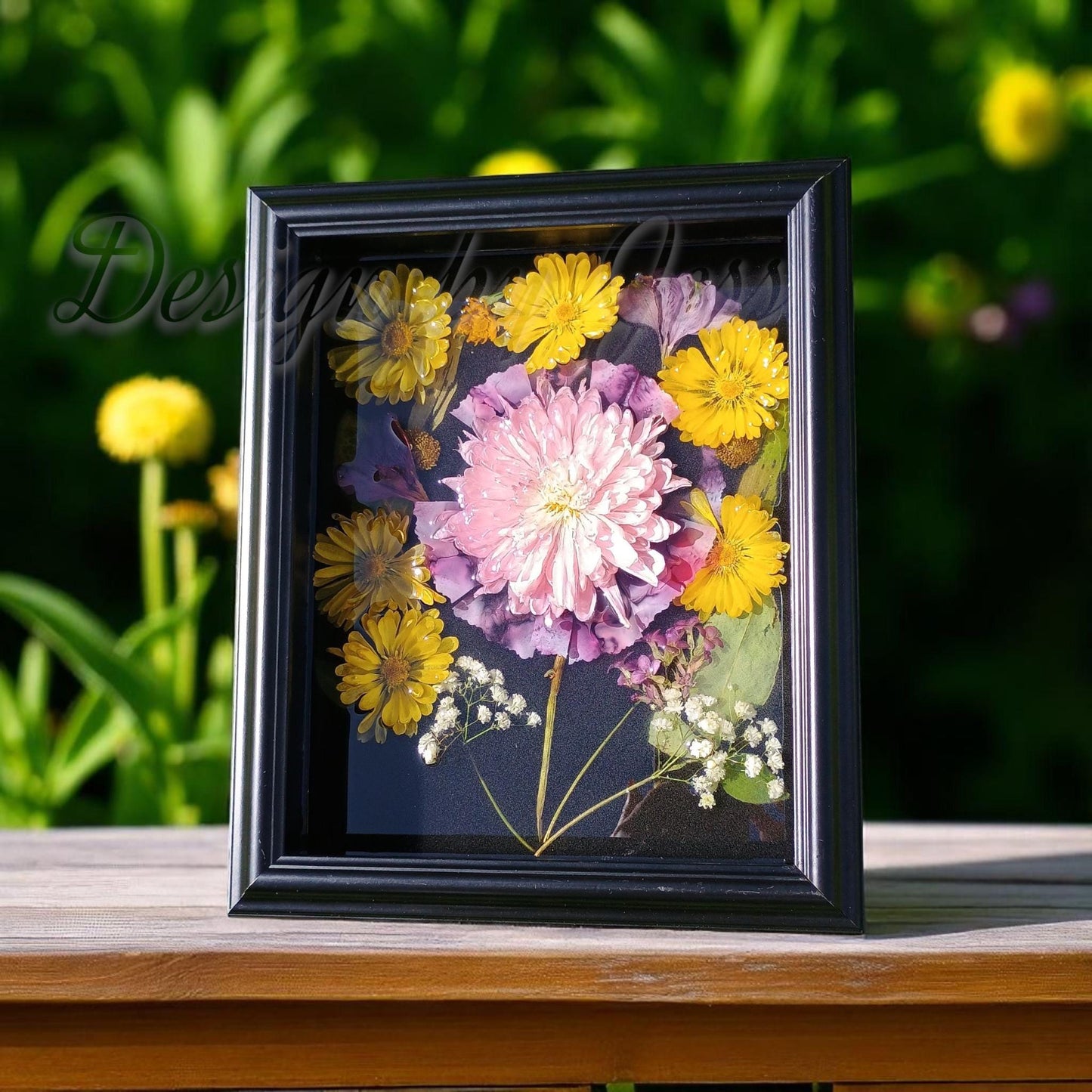 Framed flowers in resin nestled in a black wood shadow box a wooden surface with a garden background