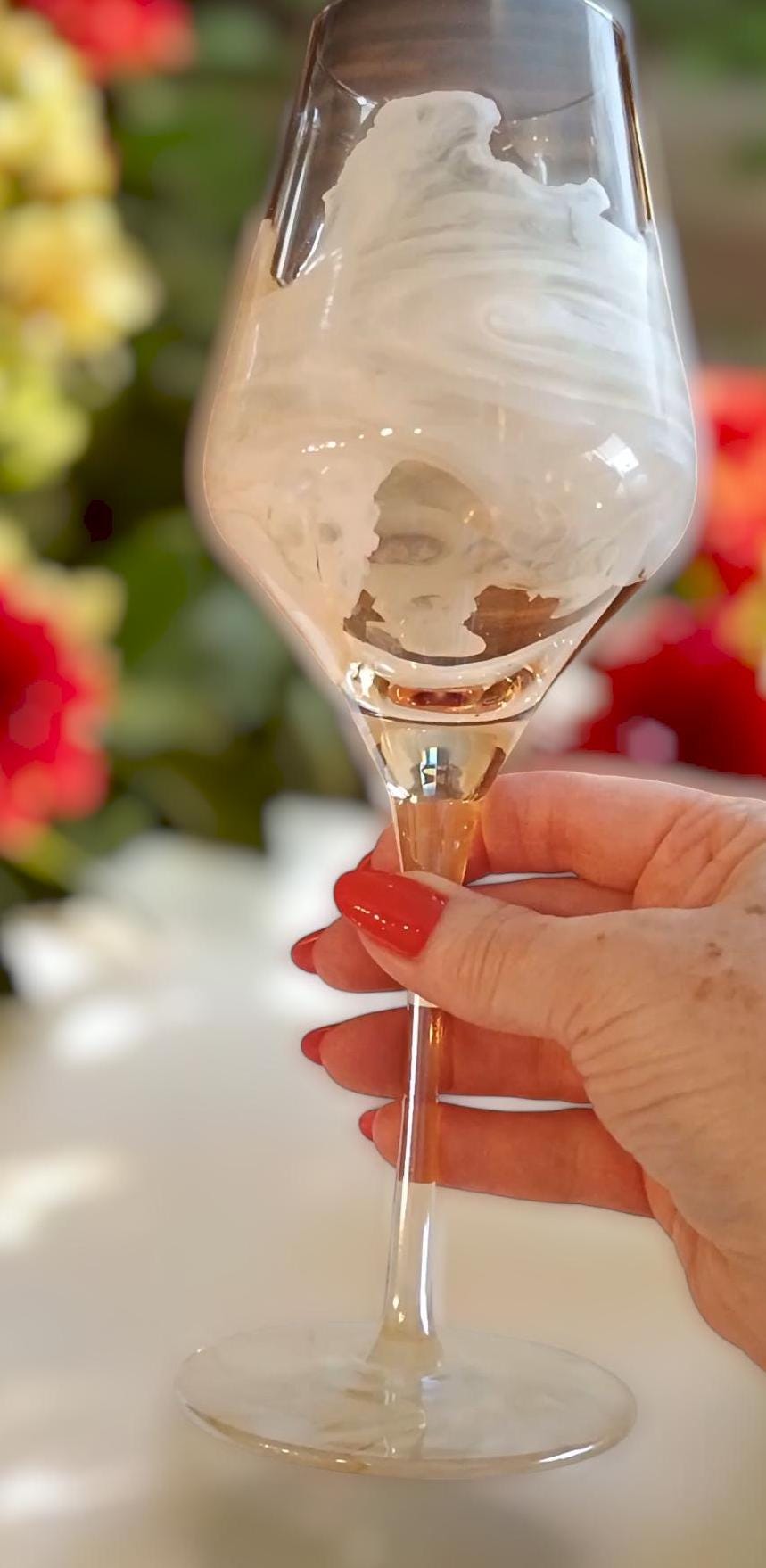 Hand holding a amber wine glass with a white marble like design and floral background