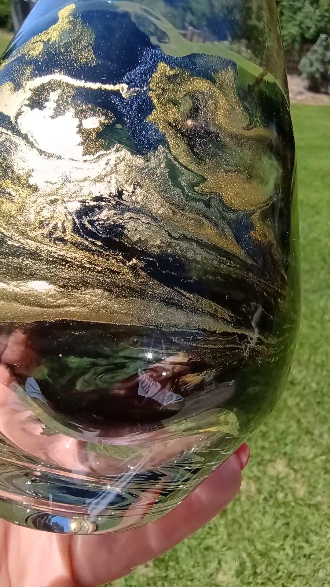 Glass cup with artistic design held by a hand against a grassy background