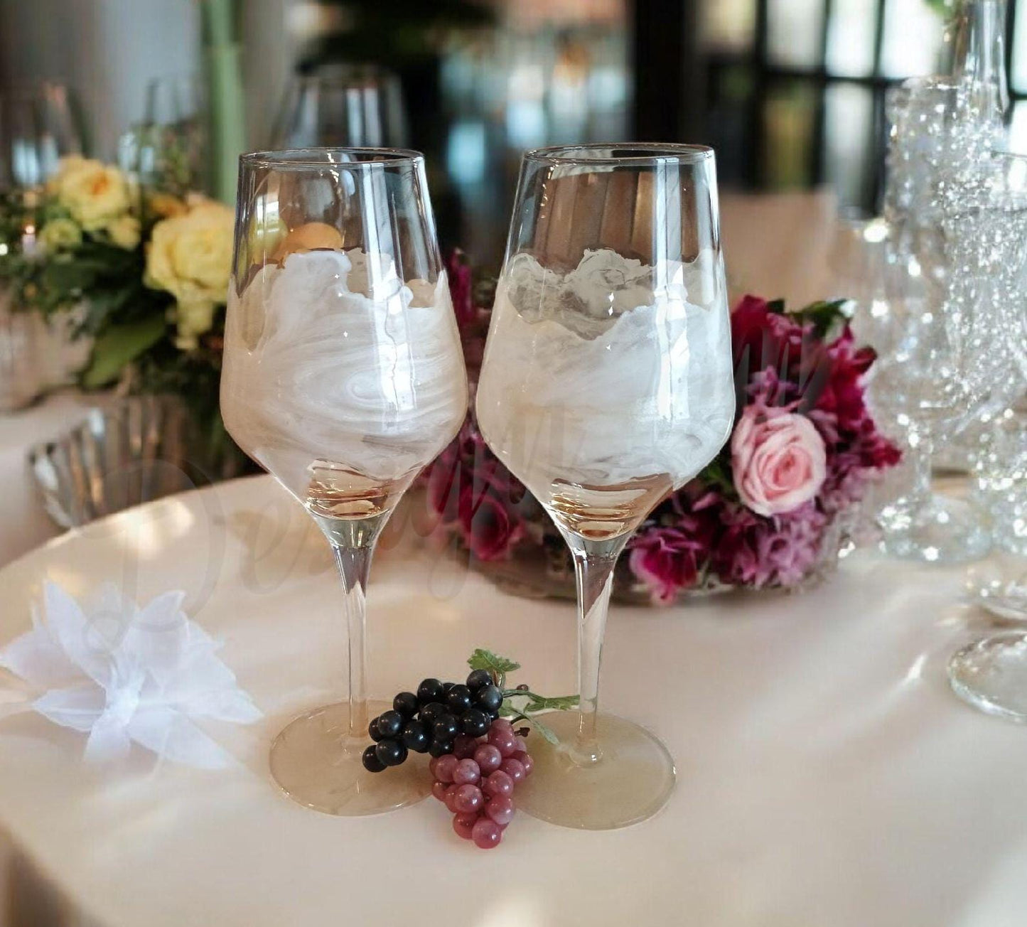Two decorated wine glasses on a table with flowers and grapes a Style by Jess