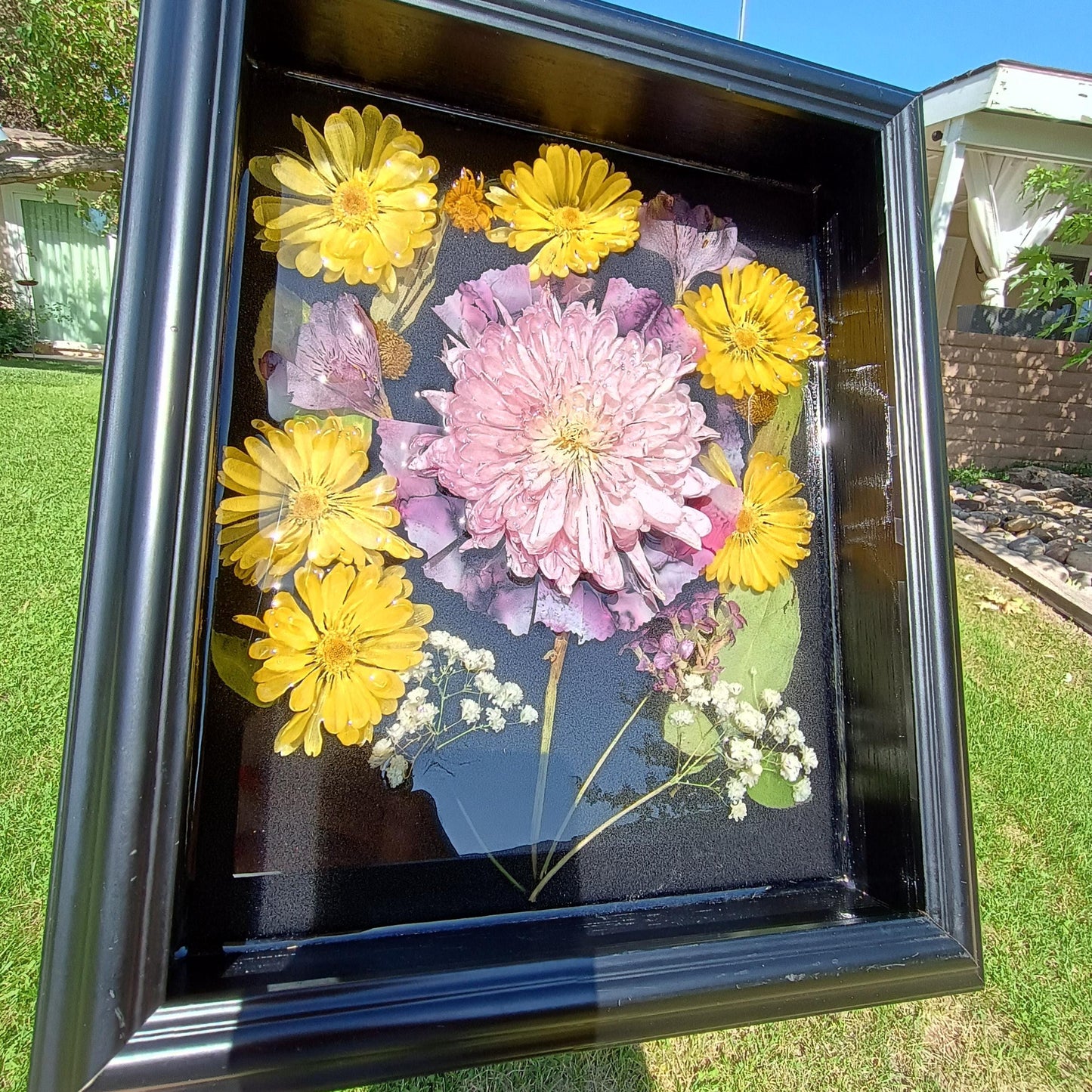 Framed arrangement of dried flowers with yellow and pink flowers on a grassy background