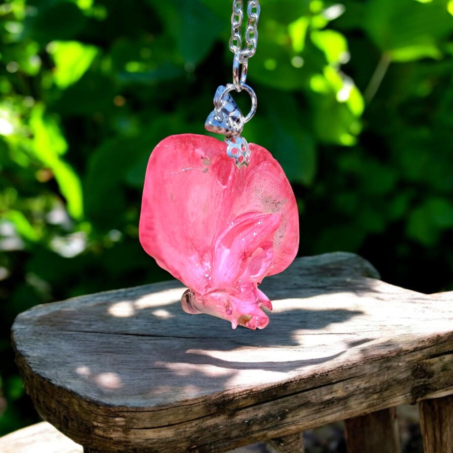 Pink glass pendant on a chain against a green leafy background