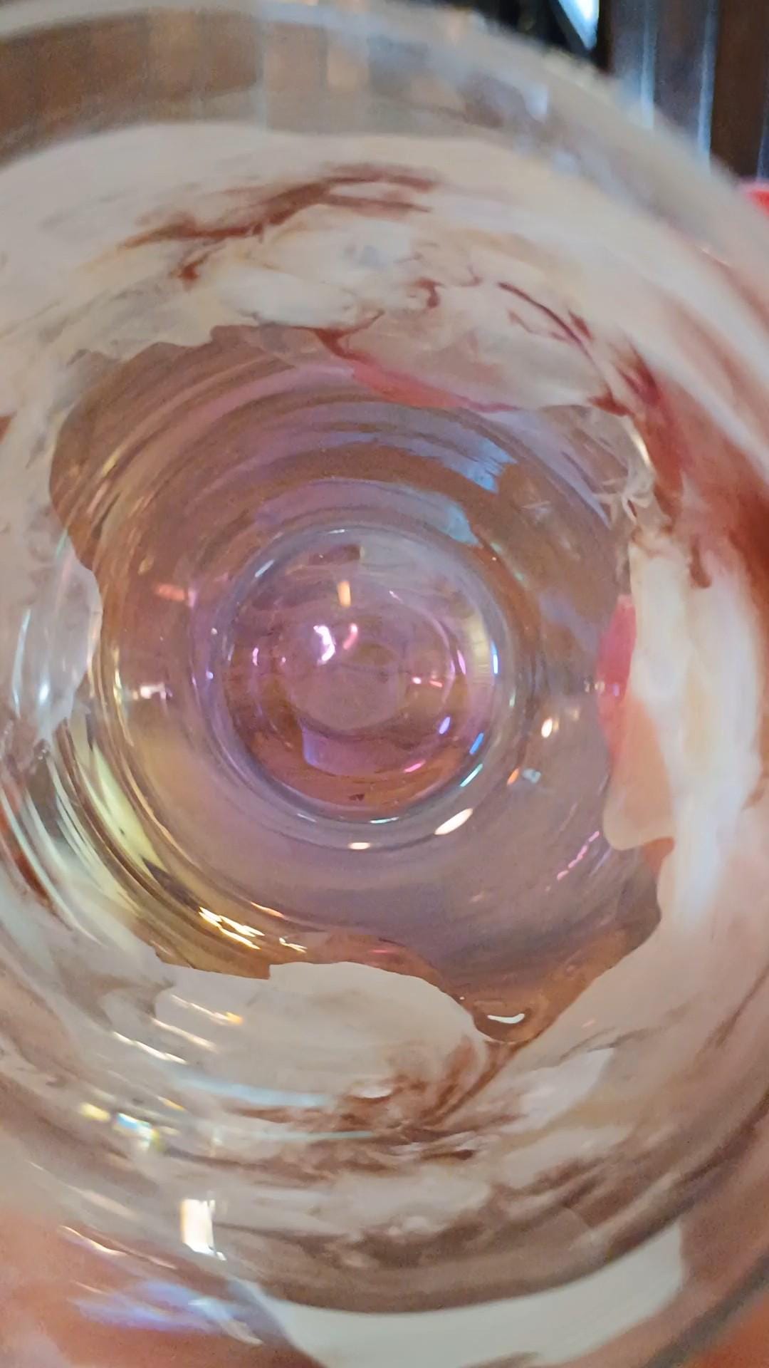 Close-up of the inside view of a hand painted resin stemless wine glass with swirling patterns with the glass tilted up as if taking a drink. 