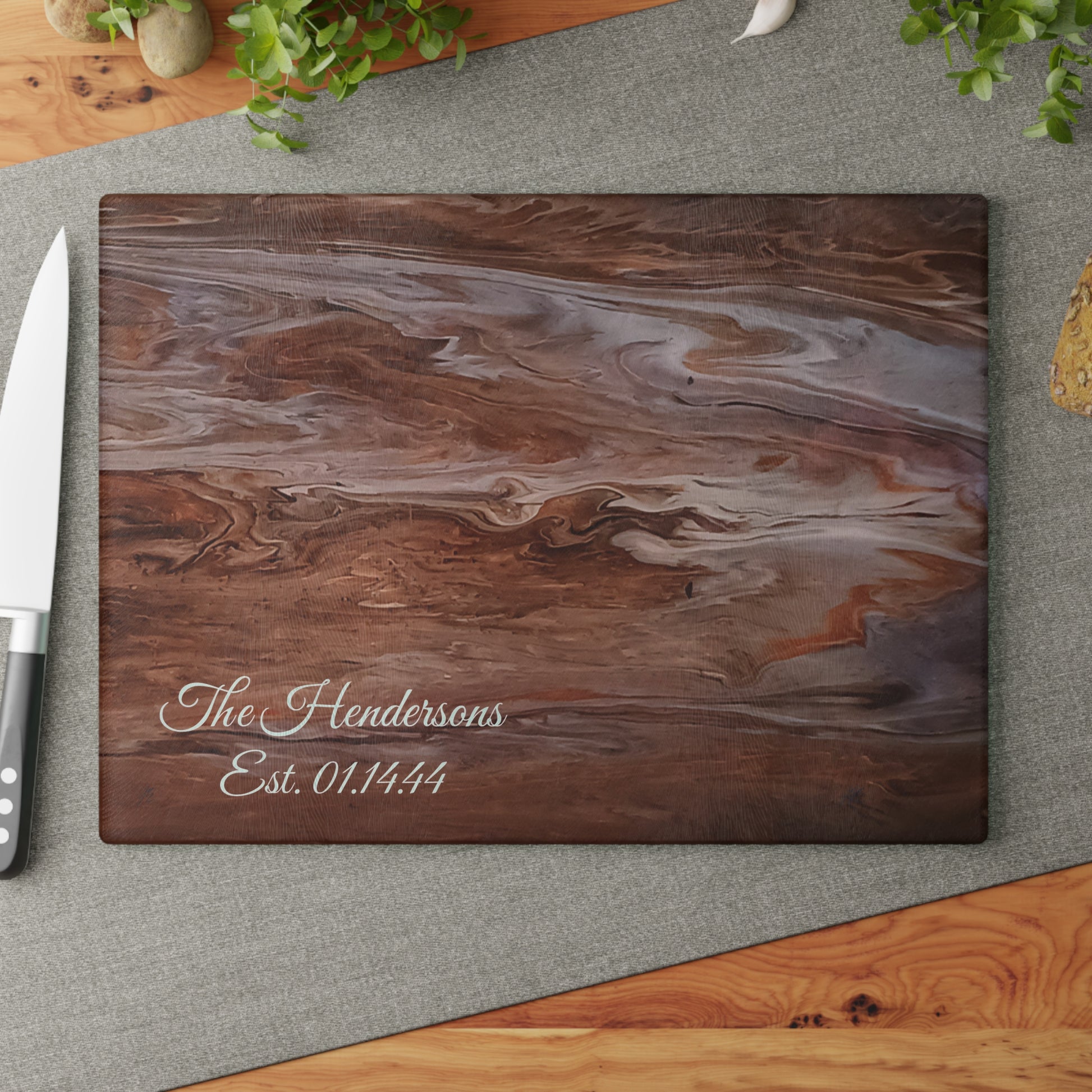 Wooden cutting board with marbled pattern and 'The Hendersons Est. 01.14.44' text on a gray surface.