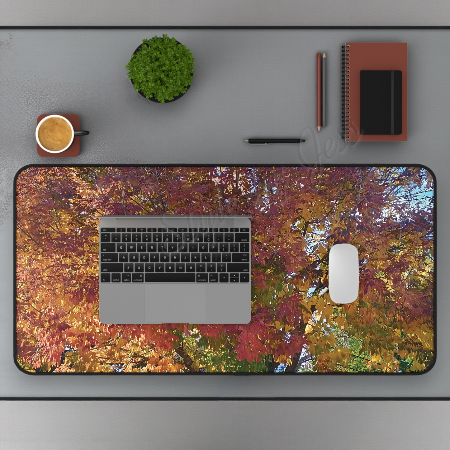 Desk setup with a large desk mat featuring autumn leaves, laptop, mouse, and office supplies minimalist decor.