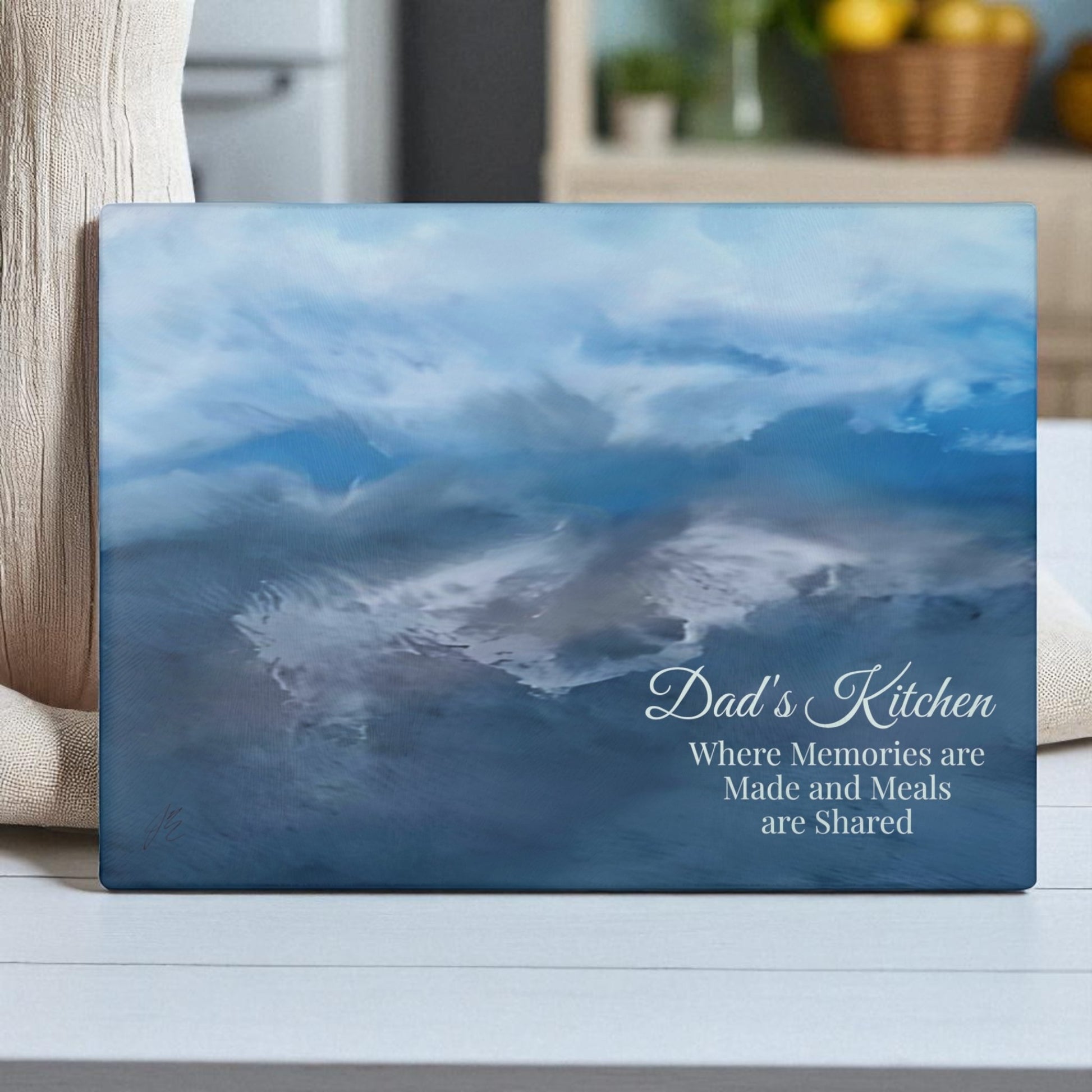 Decorative glass cutting board with a blue sky and cloud design, featuring text 'Dad's Kitchen' on a white surface.