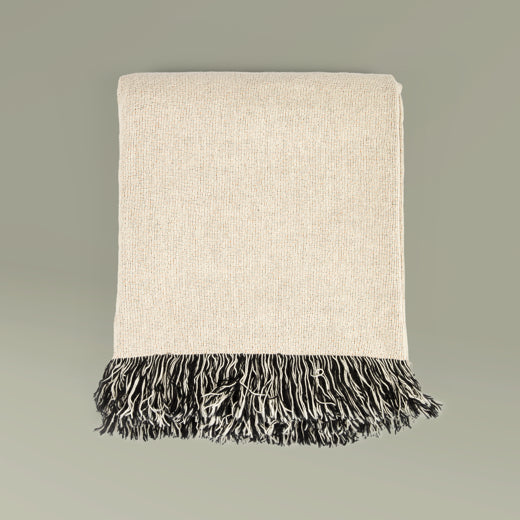 Beige throw blanket with black fringe on a gray background