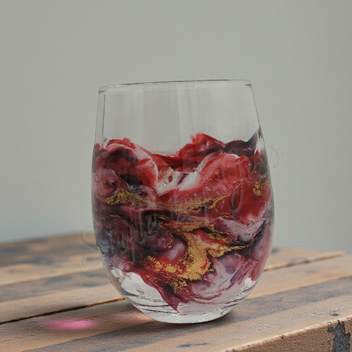 Stemless Wine Glass with marbled red, white, and gold design on a wooden surface