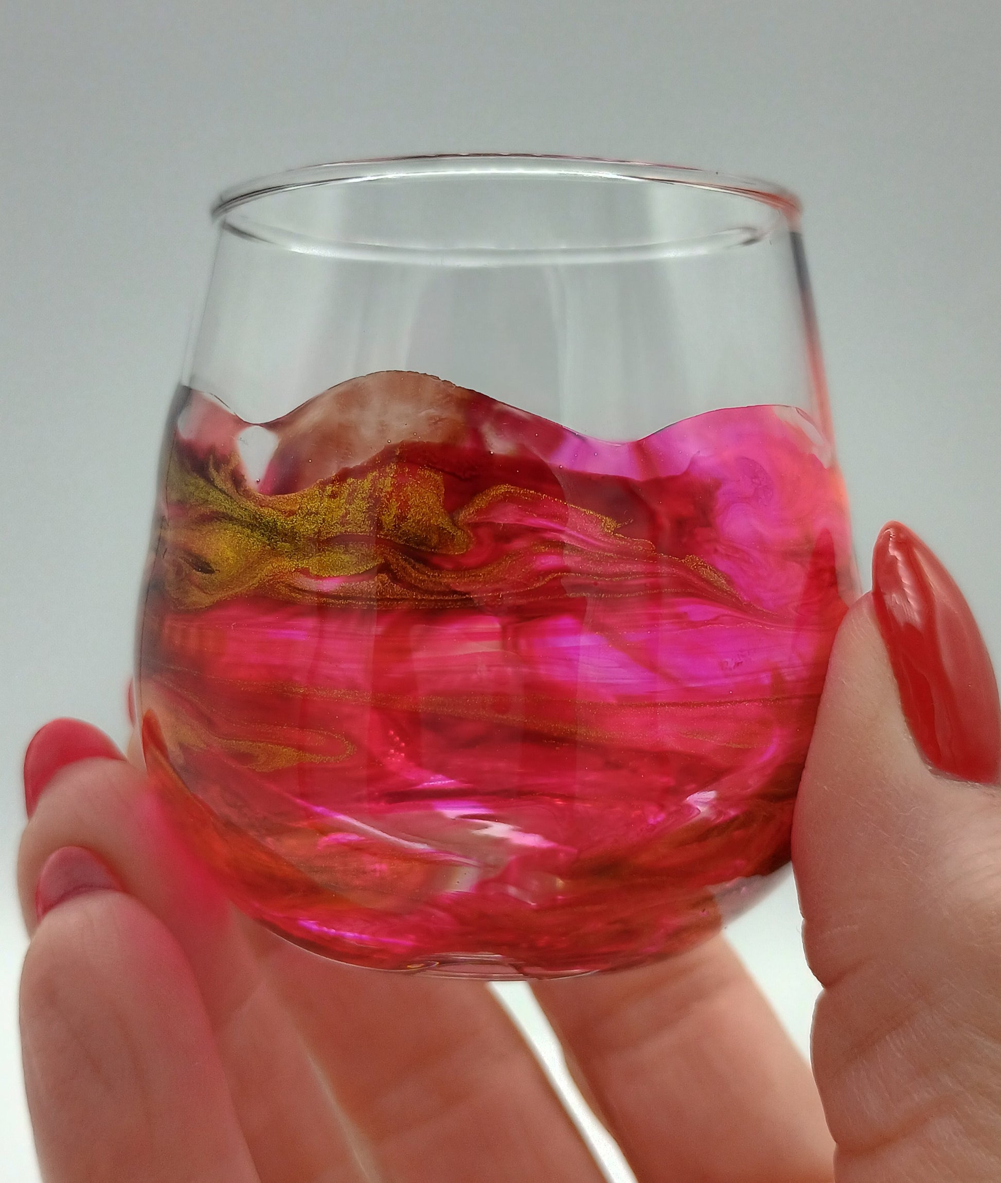 Hand holding a glass with pink and red liquid against a gray background