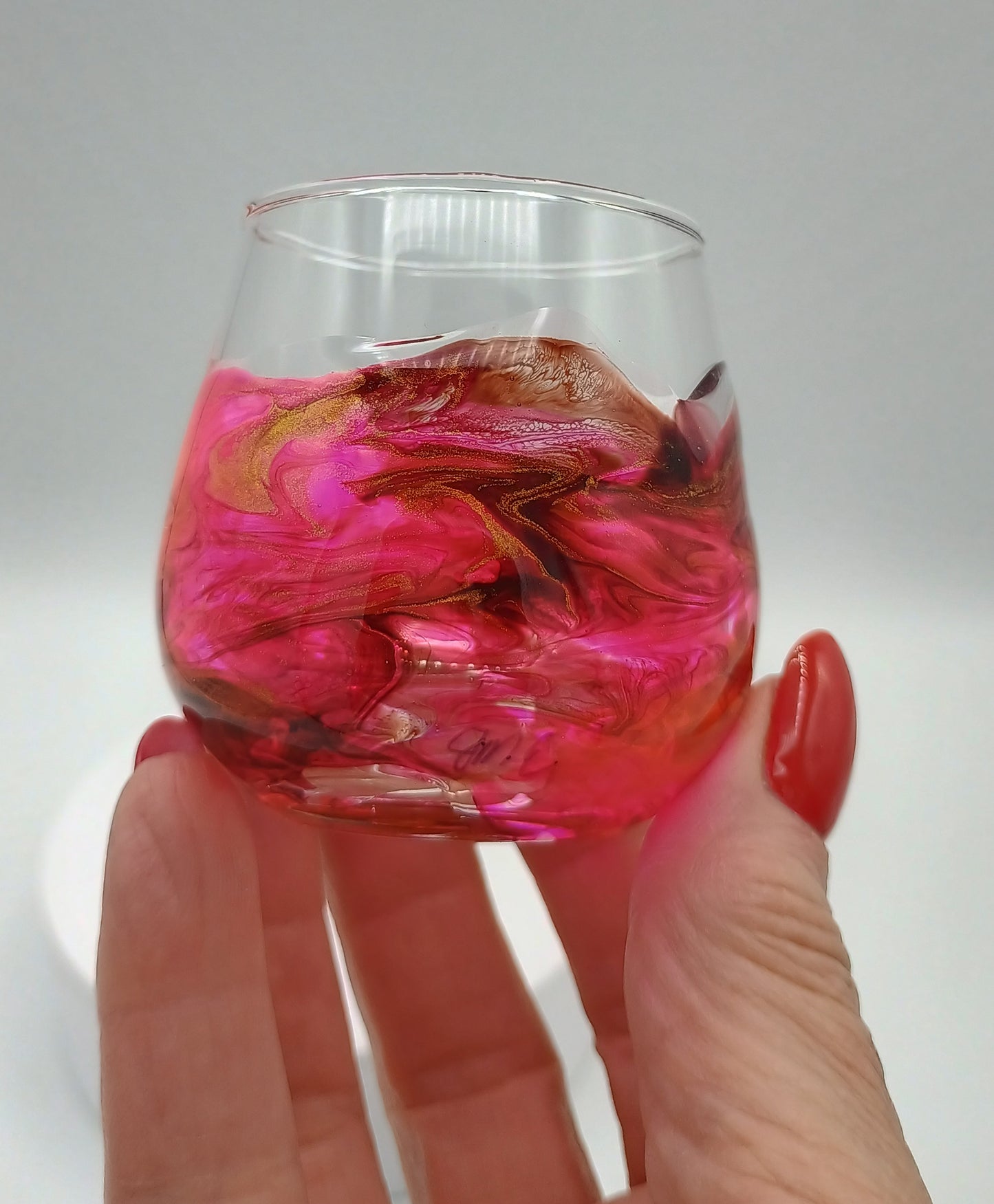 Hand holding a glass with abstract art resin applied to the shot glass giving it a custom red and gold marbled look. A Style by Jess at Gotta Have It Design