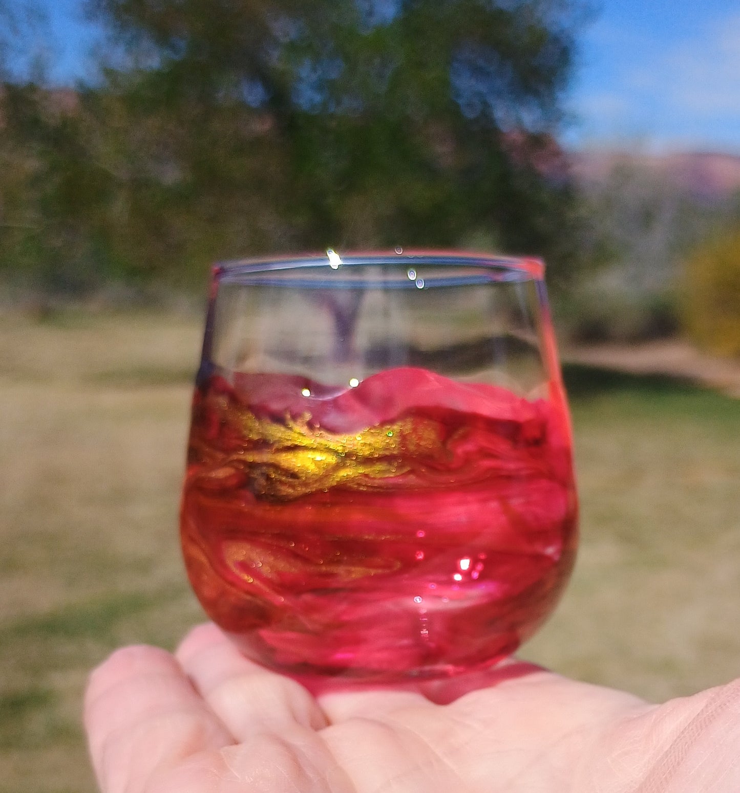 Hand holding a red and gold marbled shot glass against a blurred outdoor background a Style By Jess at Gotta Have It Design