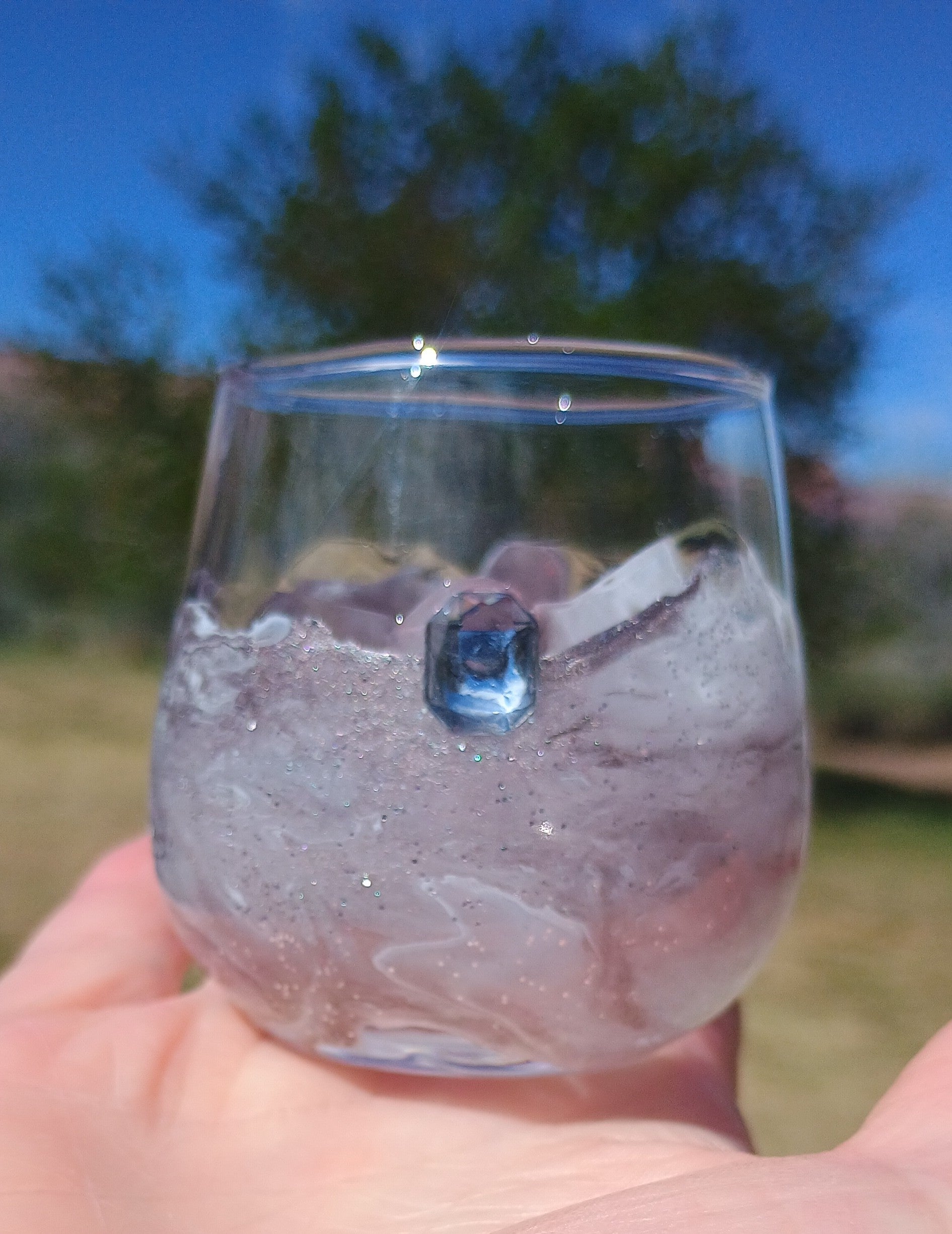 Clear Shot glass with a small gem highlighting the artistic resin design around the glass in front of a blurred natural background