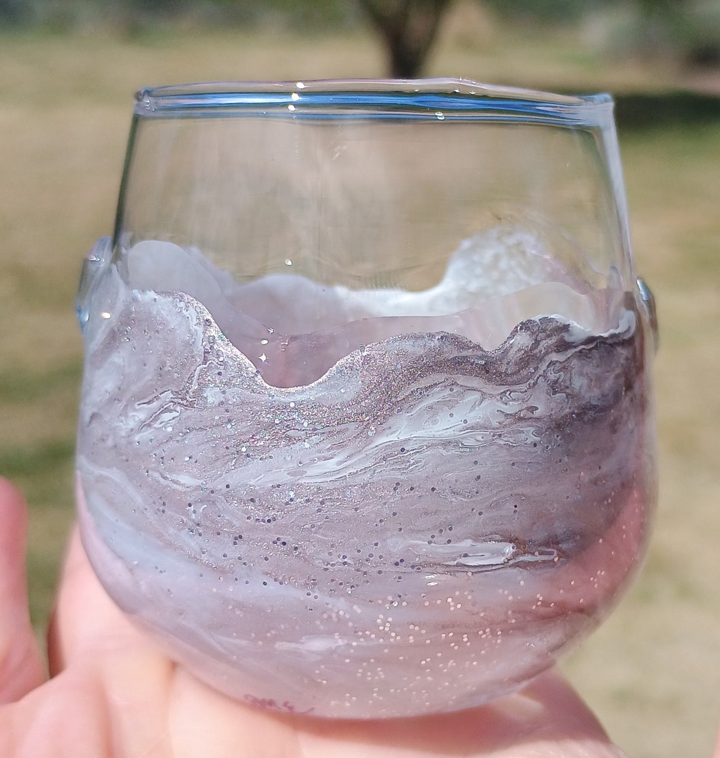 Shot glass with marbled design held in hand against a blurred natural background great as a bar accessory.