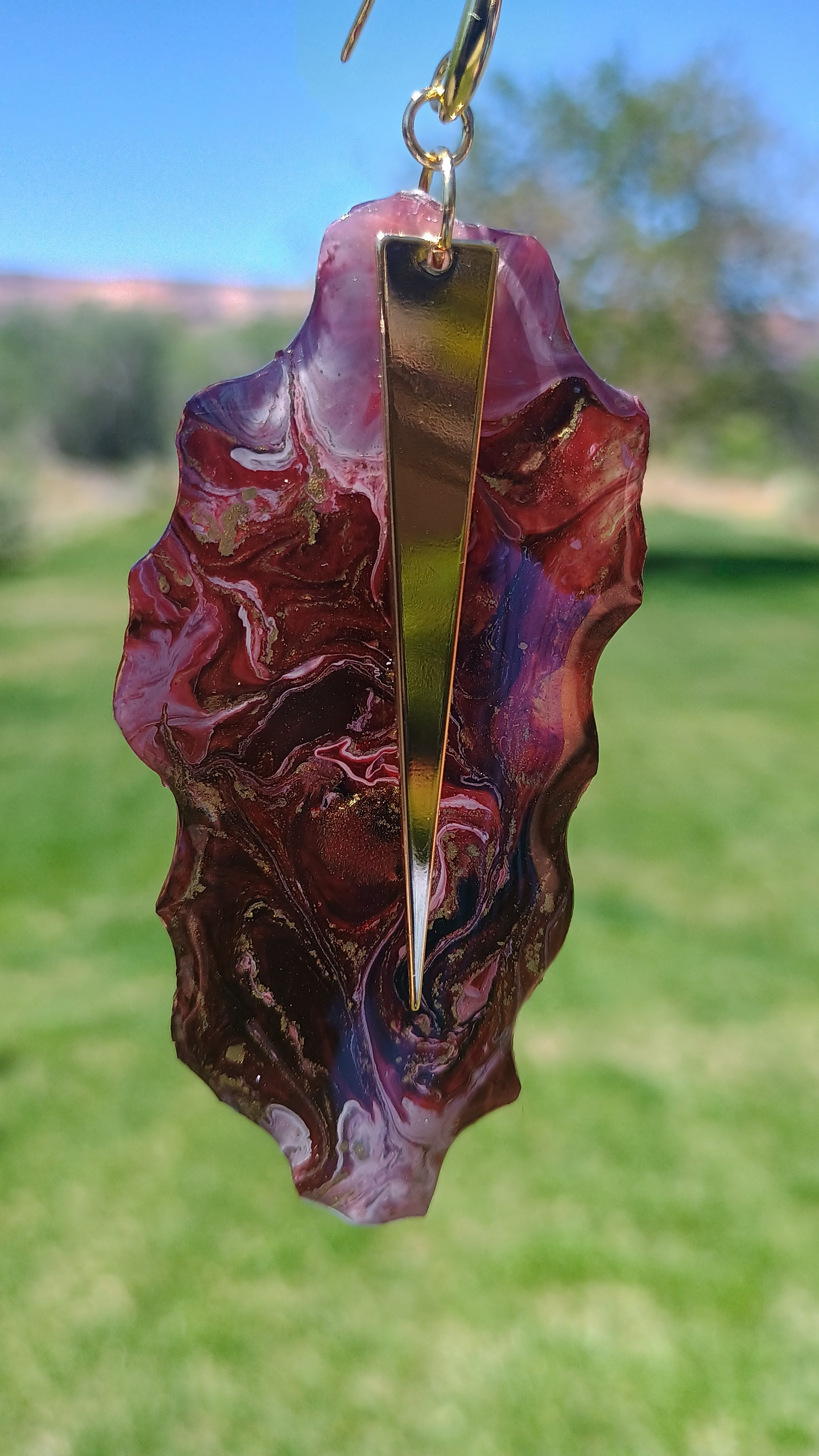 Marbled wine red and designer gold earring against a blurred green outdoor background