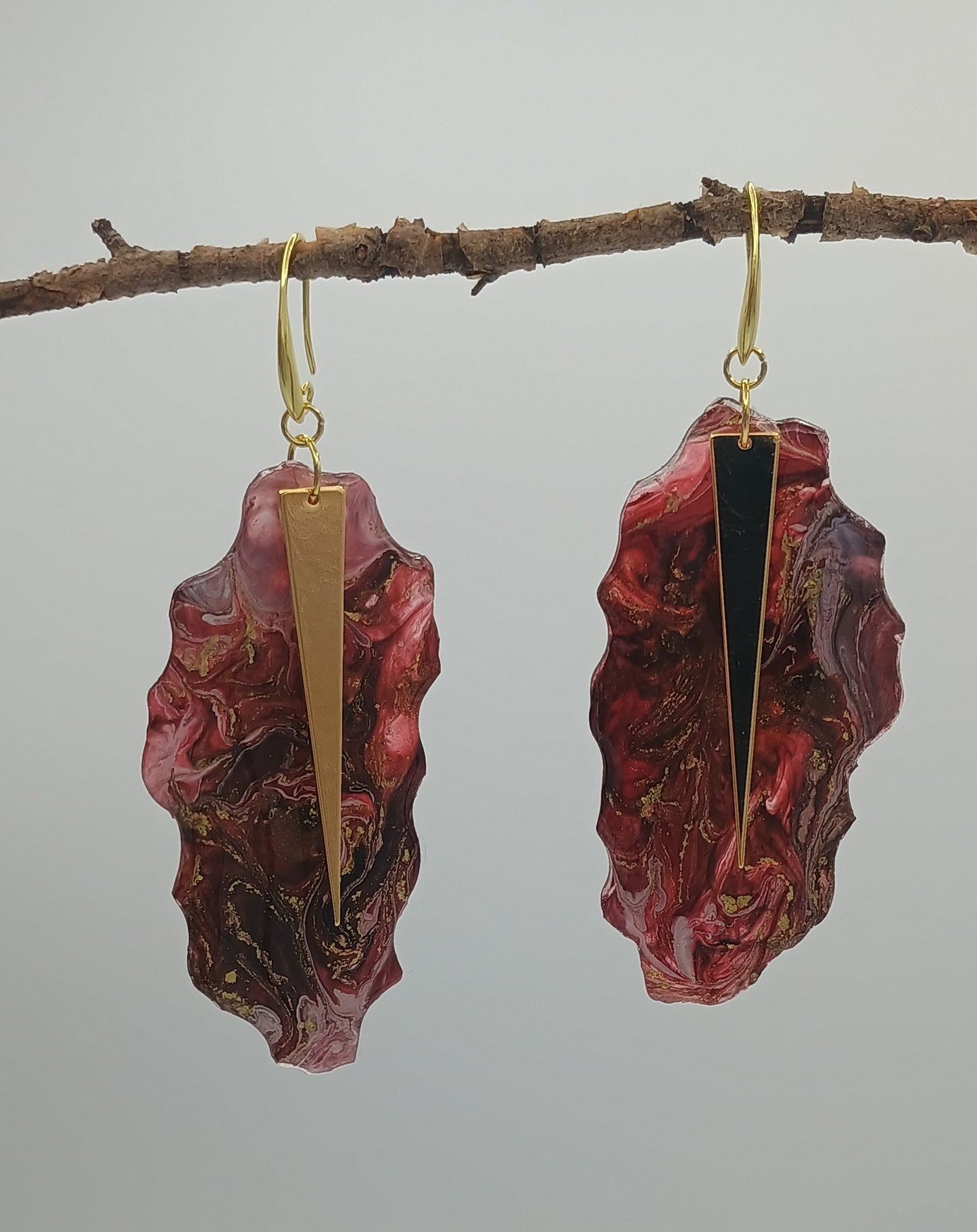 Marbled red and gold handmade earrings on a branch against a gray background a Style By Jess